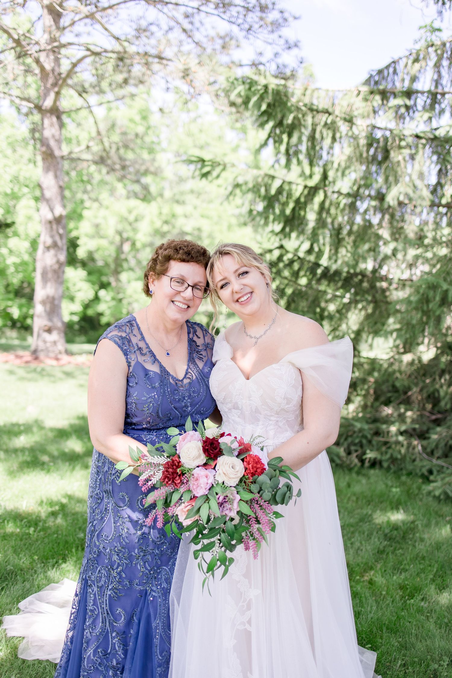 Wedding party members holding vibrant bouquets of pink and red flowers in outdoor setting.
