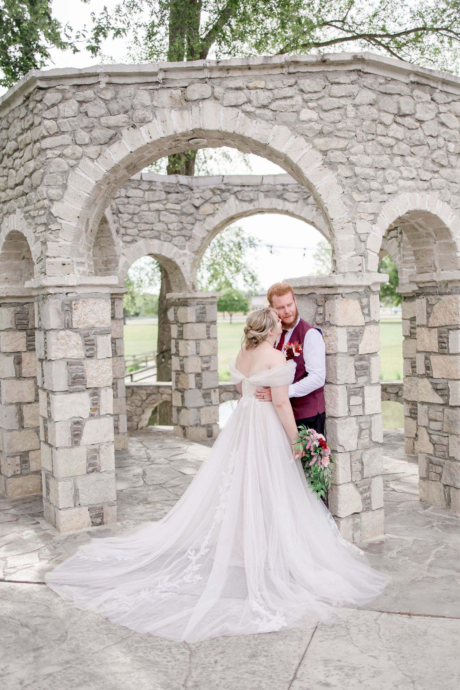 Wedding couple photographed through multiple stone archways in an elegant outdoor setting.