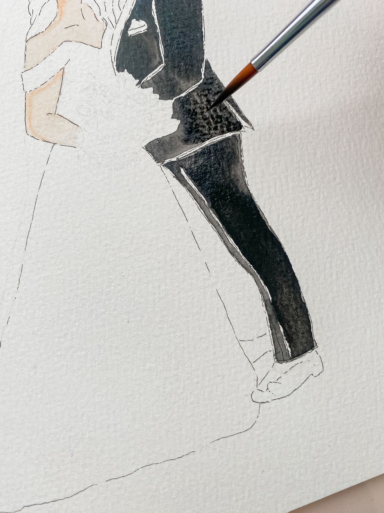 A paintbrush applies black watercolor paint to create delicate outlines on white paper.