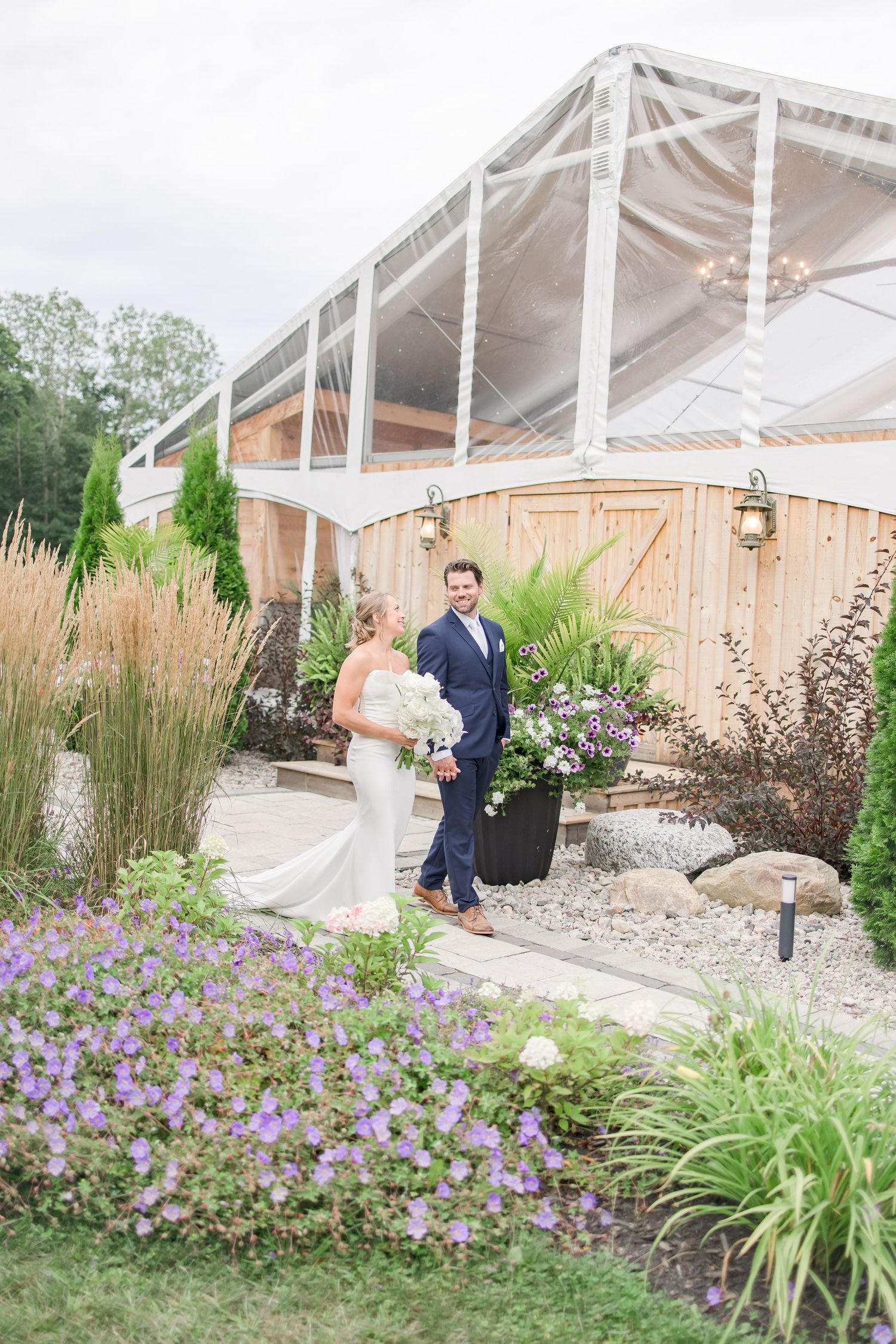 Garden wedding venue with white tent and purple flowers in landscaped outdoor setting.