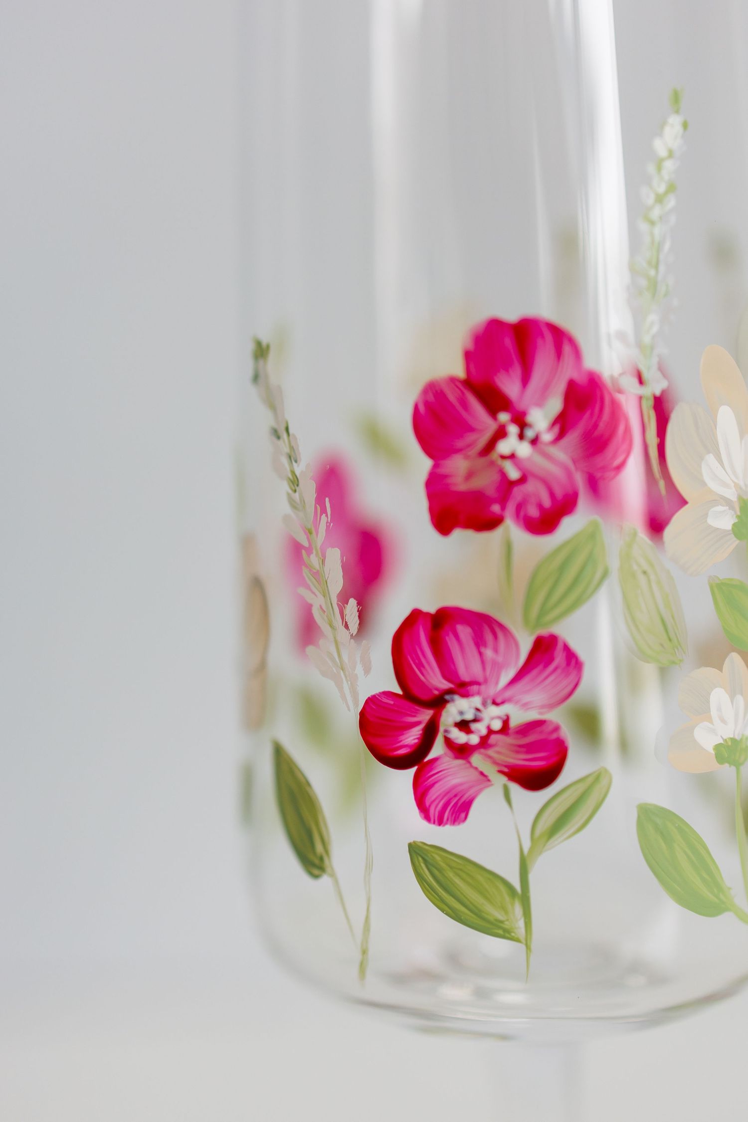 Glass jar decorated with delicate pink floral designs and green leaves creates an elegant botanical display.