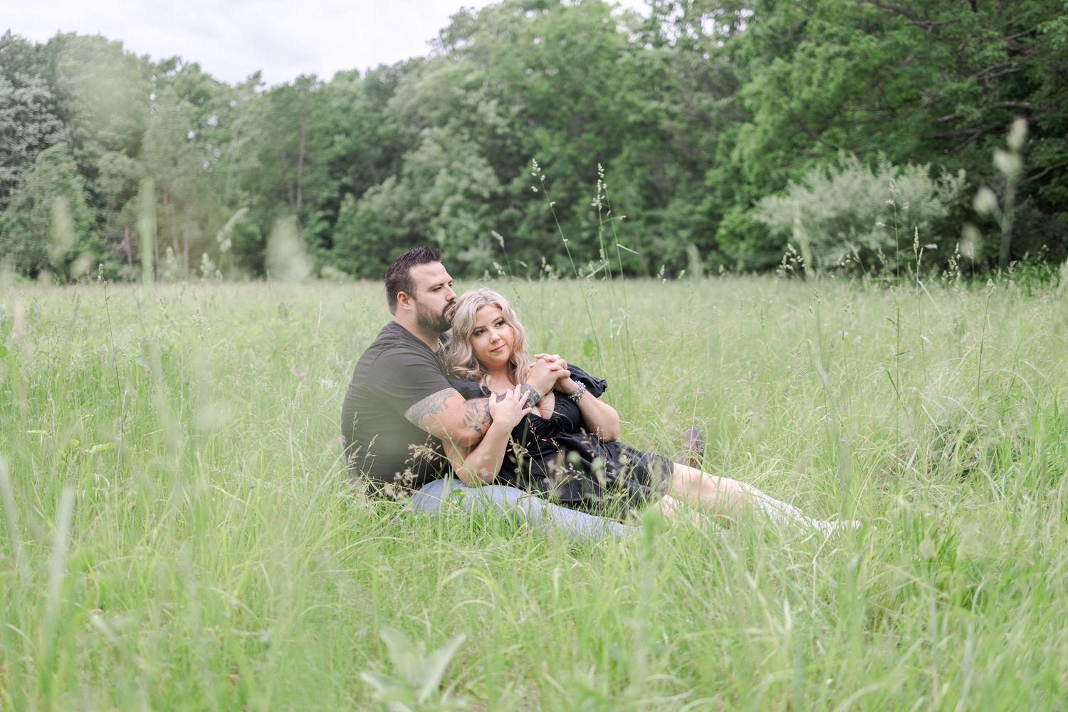 Couple relaxing together in a lush green field during a romantic outdoor photoshoot.