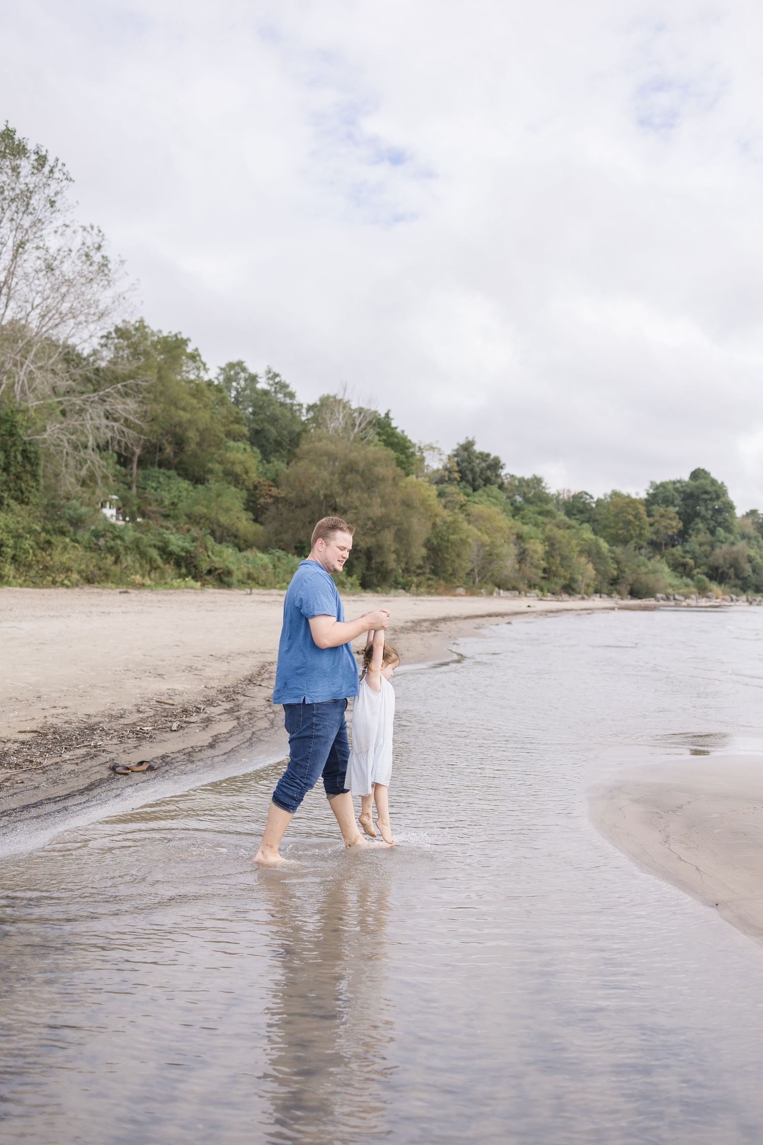 Parent and child walking together in shallow ocean water along the shoreline.