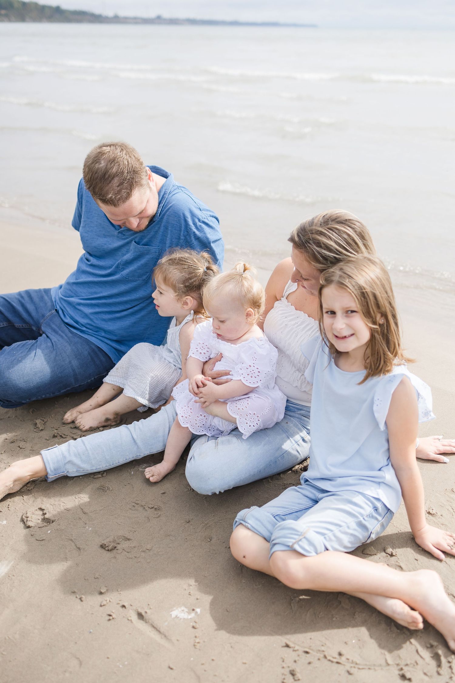 Family of four sitting together on a sandy beach near the ocean.