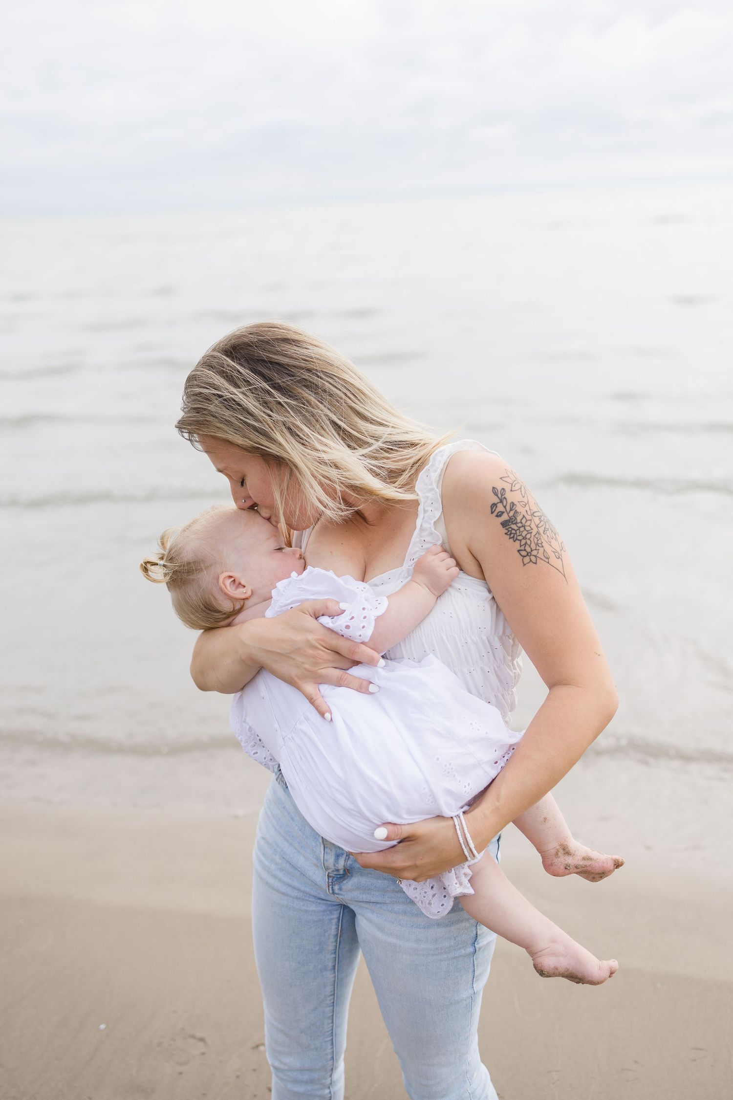 Parent holding and embracing child in white dress on a misty beach.