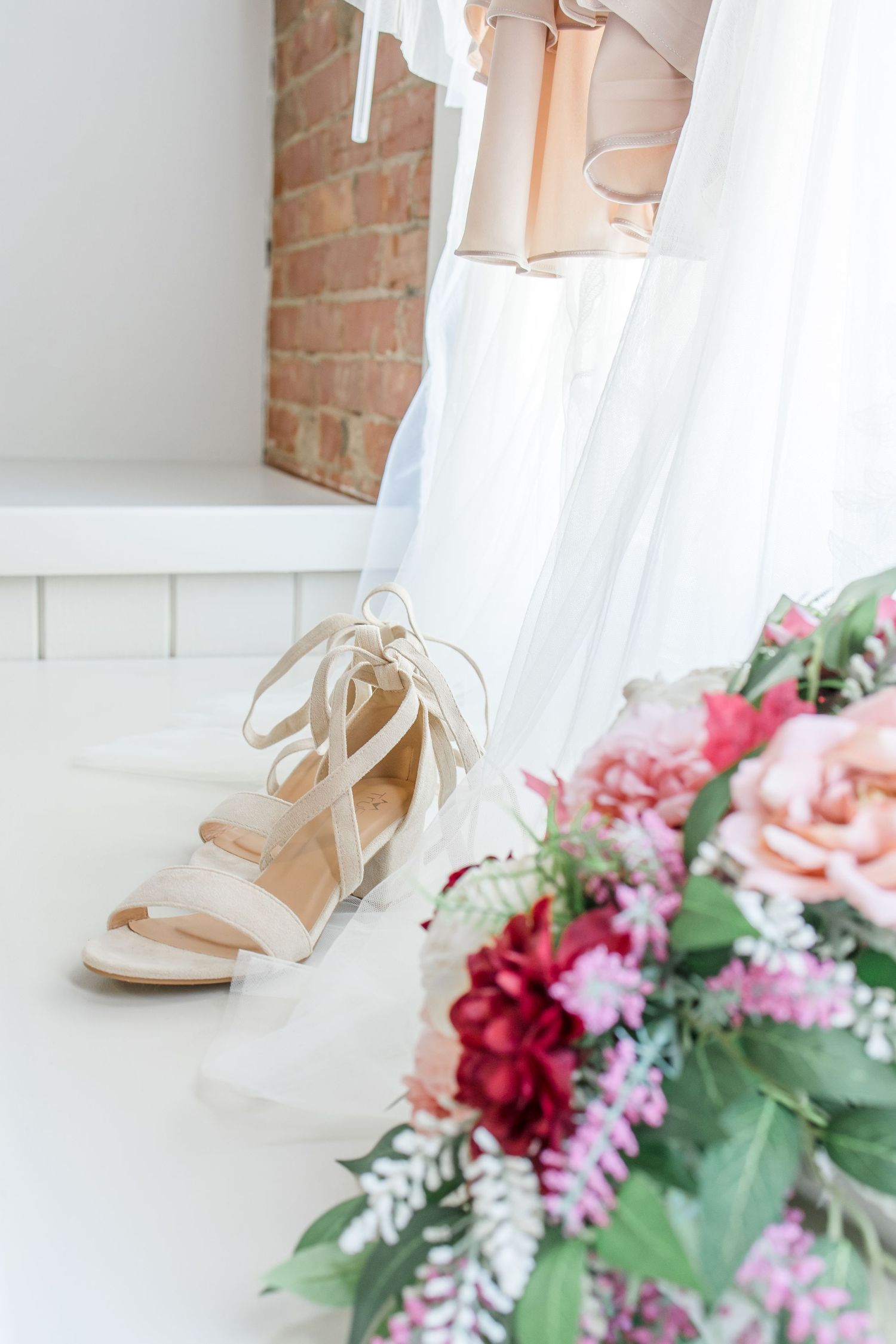 Elegant bridal shoes next to pink and red floral arrangements against a white backdrop.