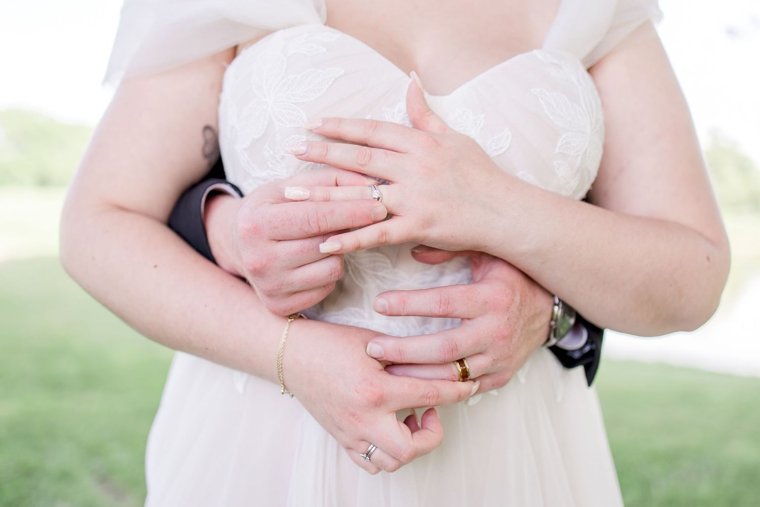 Close-up detail of hands with wedding rings against white dress.