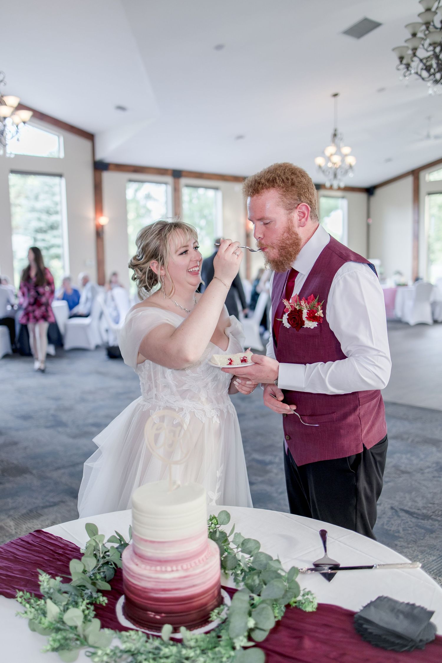 Couple sharing wedding cake cutting moment with ombre burgundy and white tiered cake.