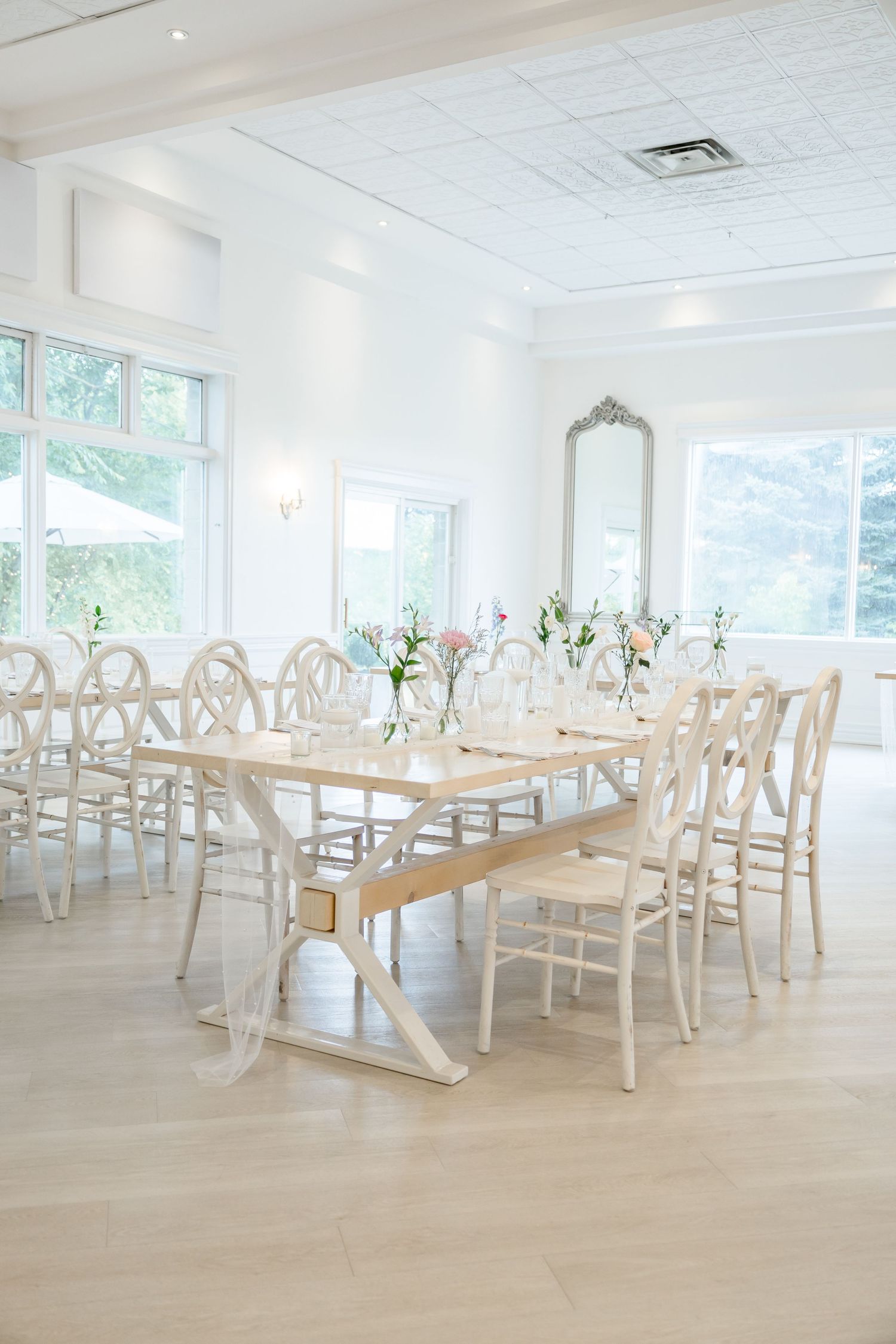 Elegant white wedding reception venue with wooden tables and chairs arranged in a bright, airy space.