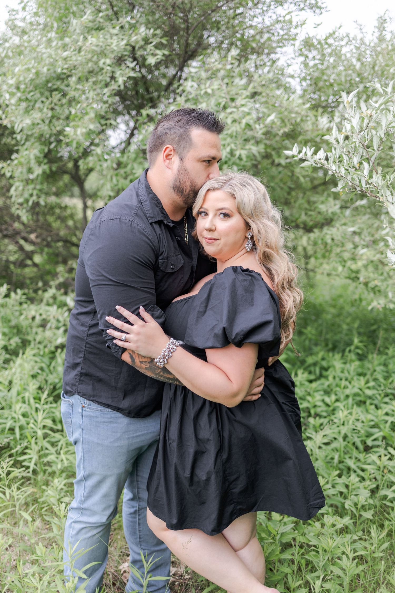 A romantic embrace captured in a lush green outdoor setting.