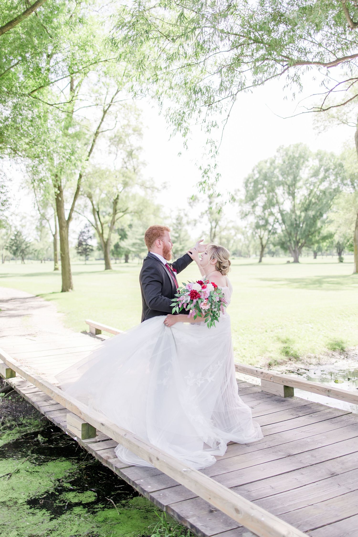 Romantic wedding scene on wooden bridge surrounded by lush greenery.
