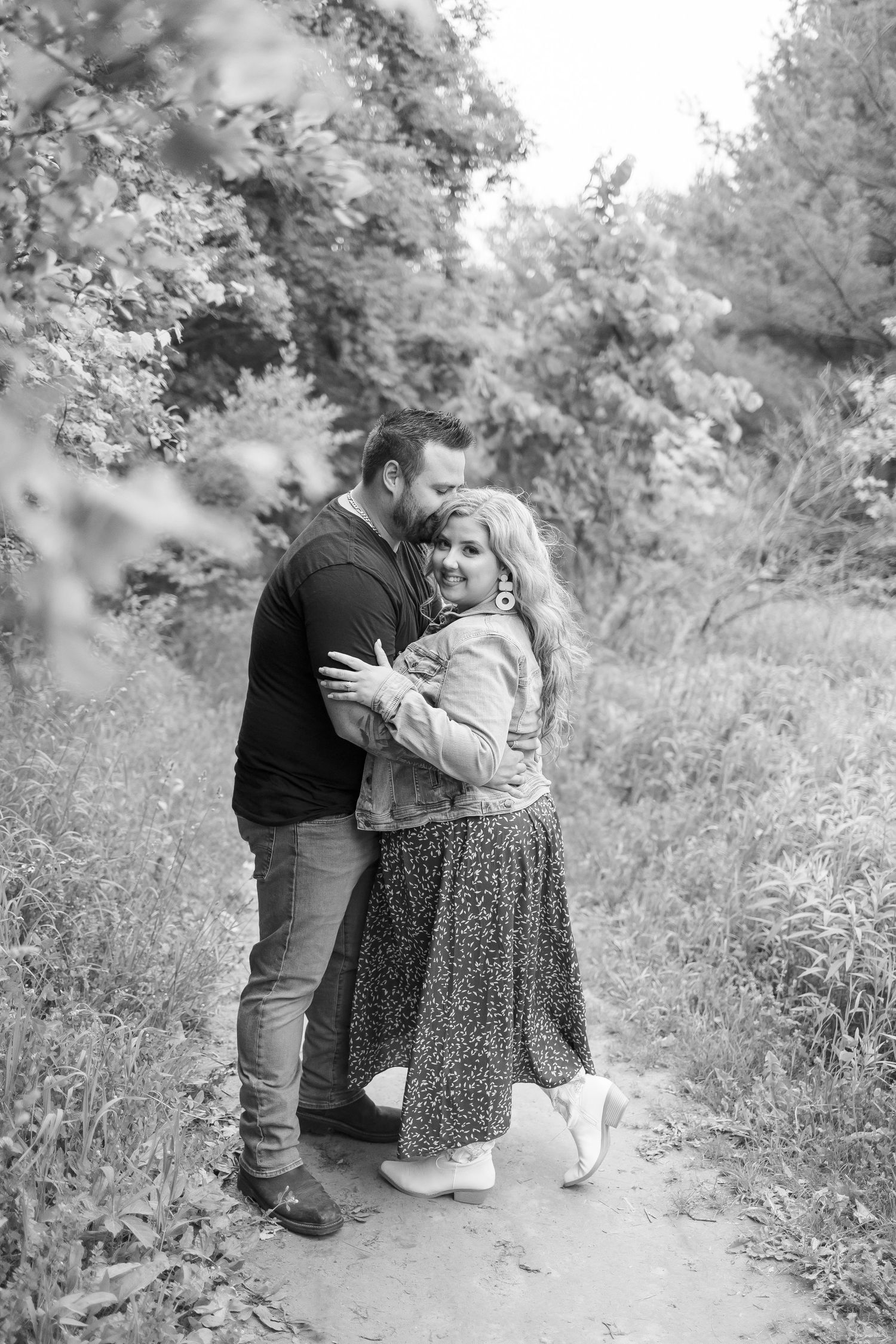 Black and white photo of a tender moment between two people on a nature path.