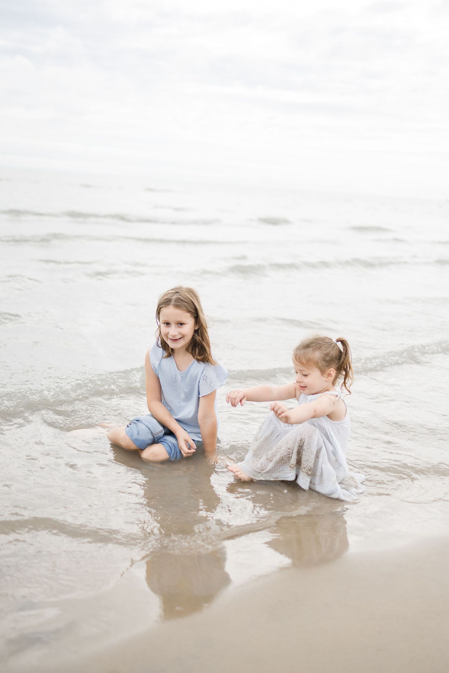 Two children play together in the shallow waves at the beach on a cloudy day.