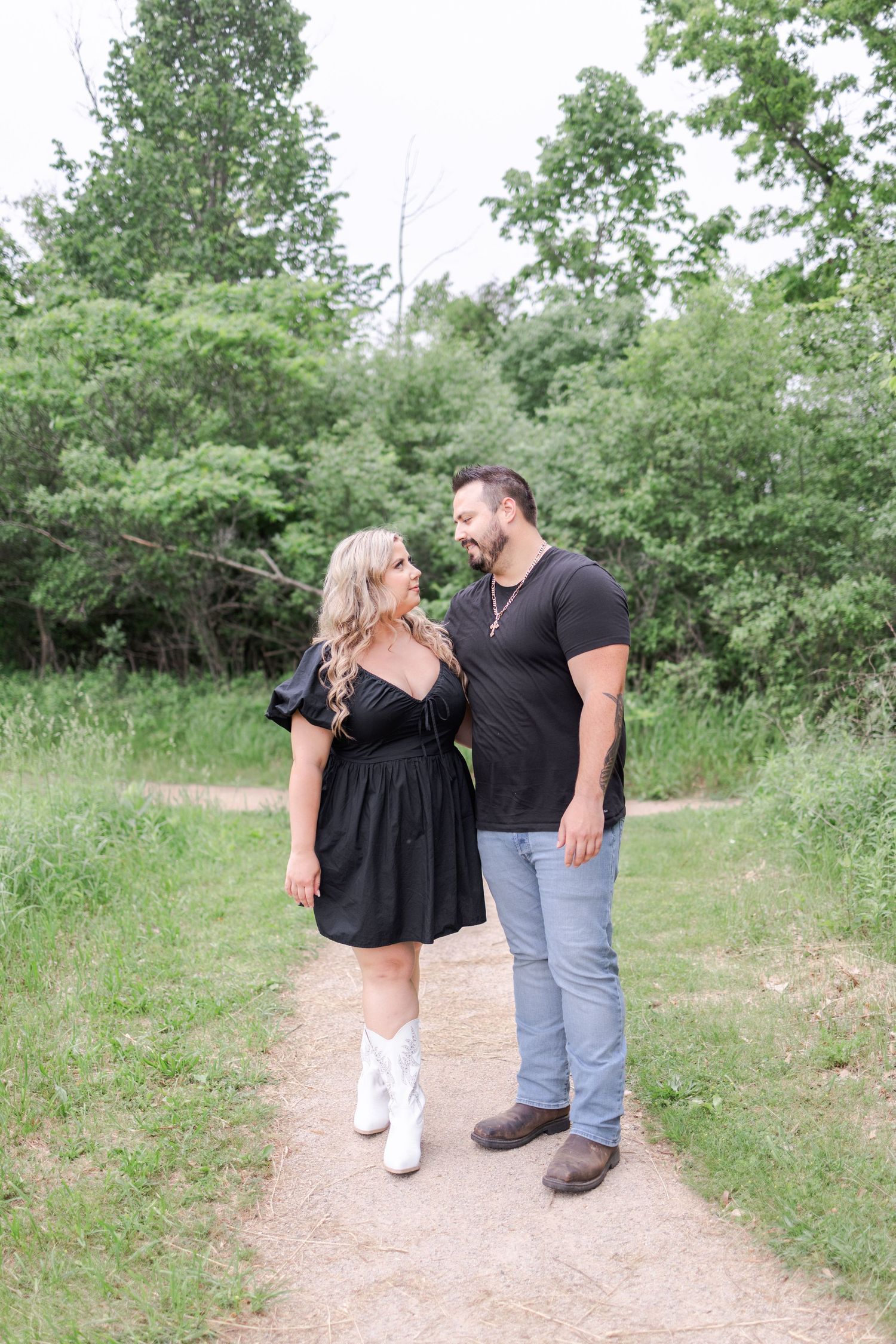 Couple strolling along a dirt path surrounded by green summer foliage.