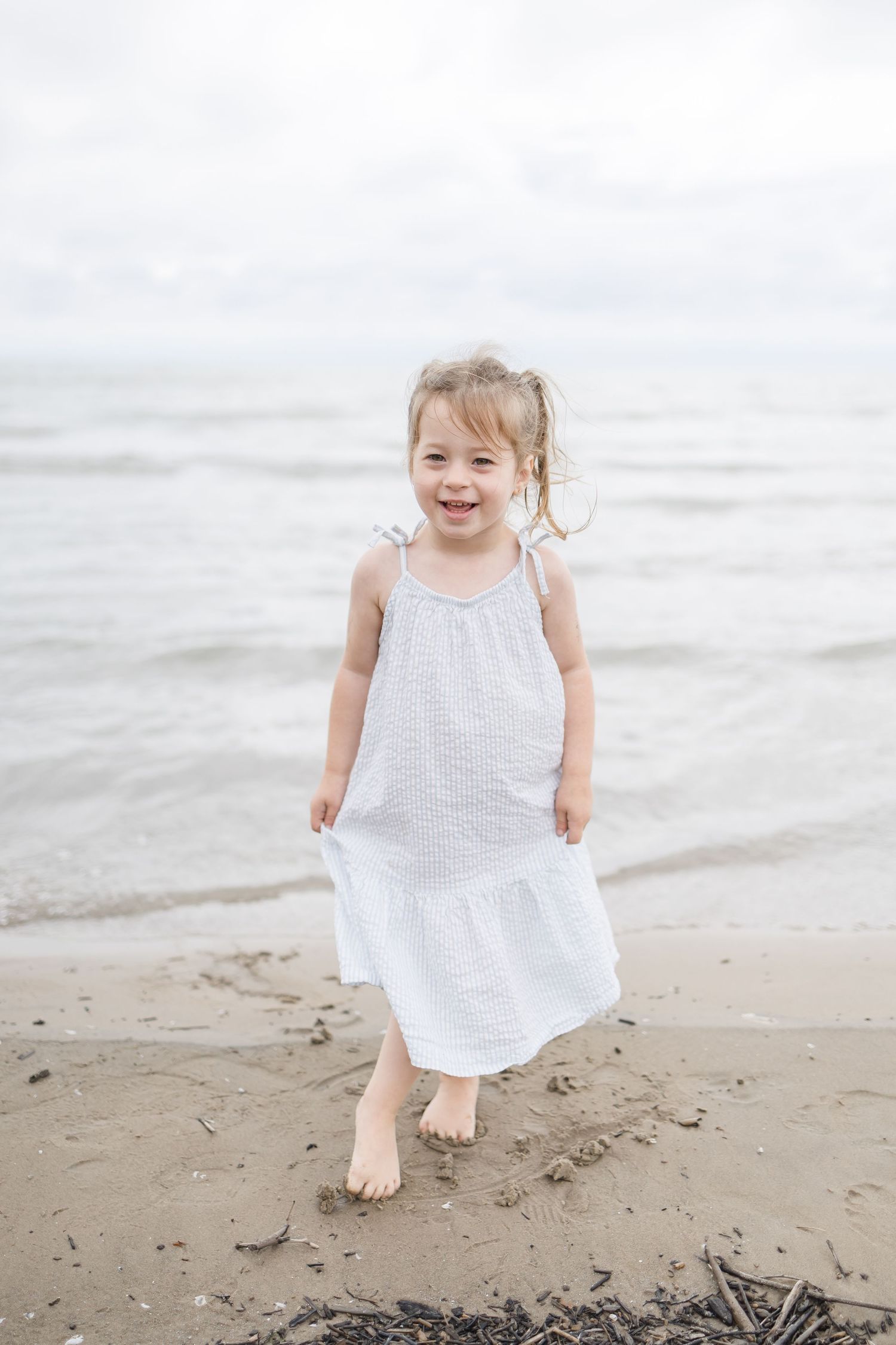 Child in white dress jumping and playing on beach sand.