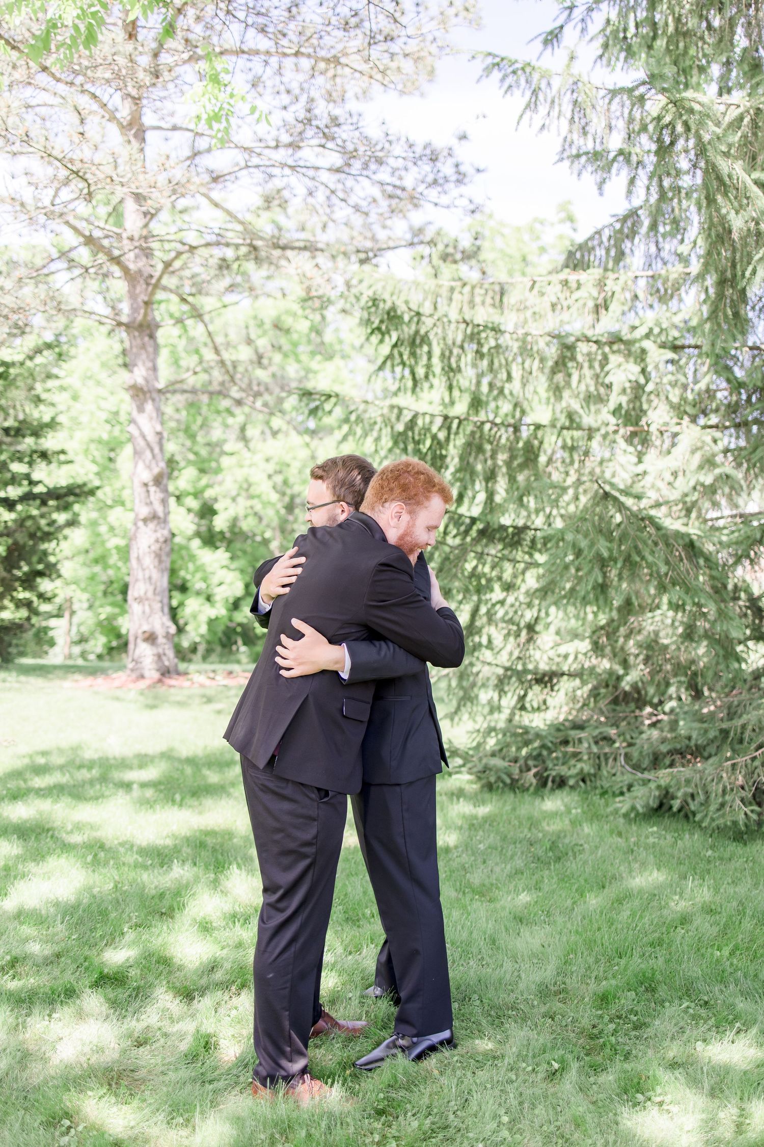 Two people in dark suits share an emotional embrace during outdoor wedding photos.