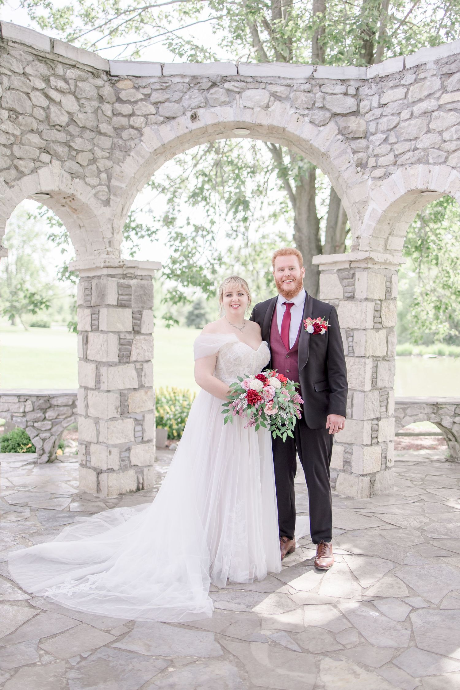 Wedding couple posing under beautiful stone archway in garden setting.