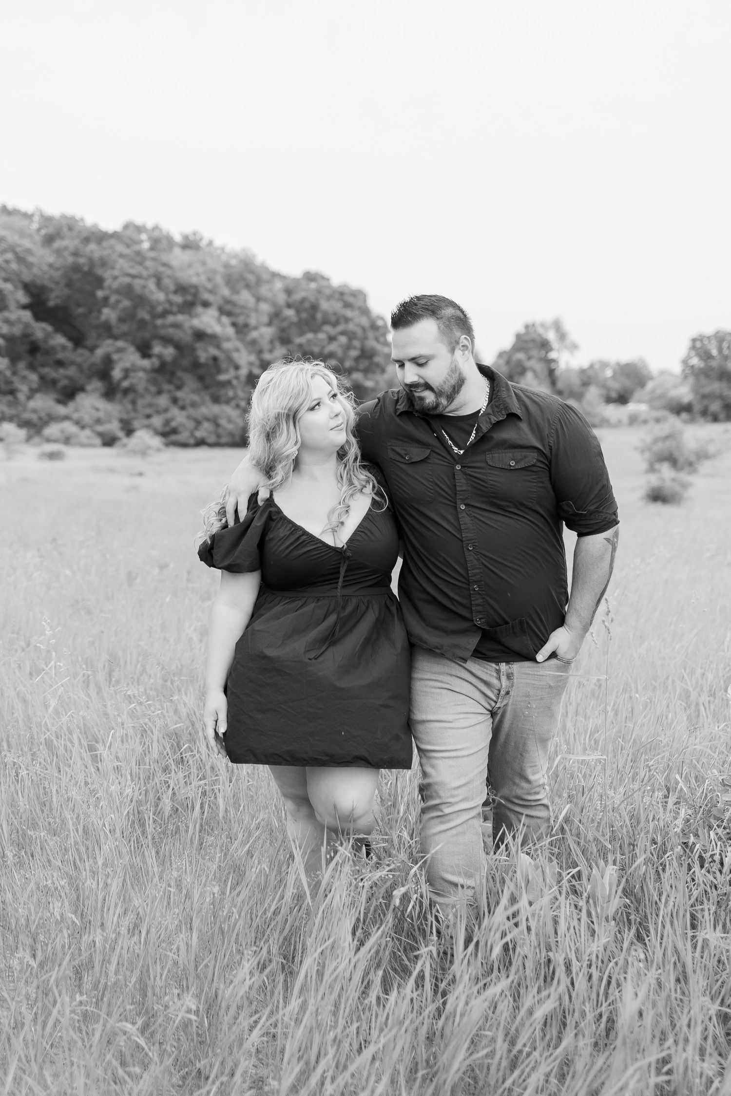 Black and white photo of a couple sharing an intimate moment in a grassy field.