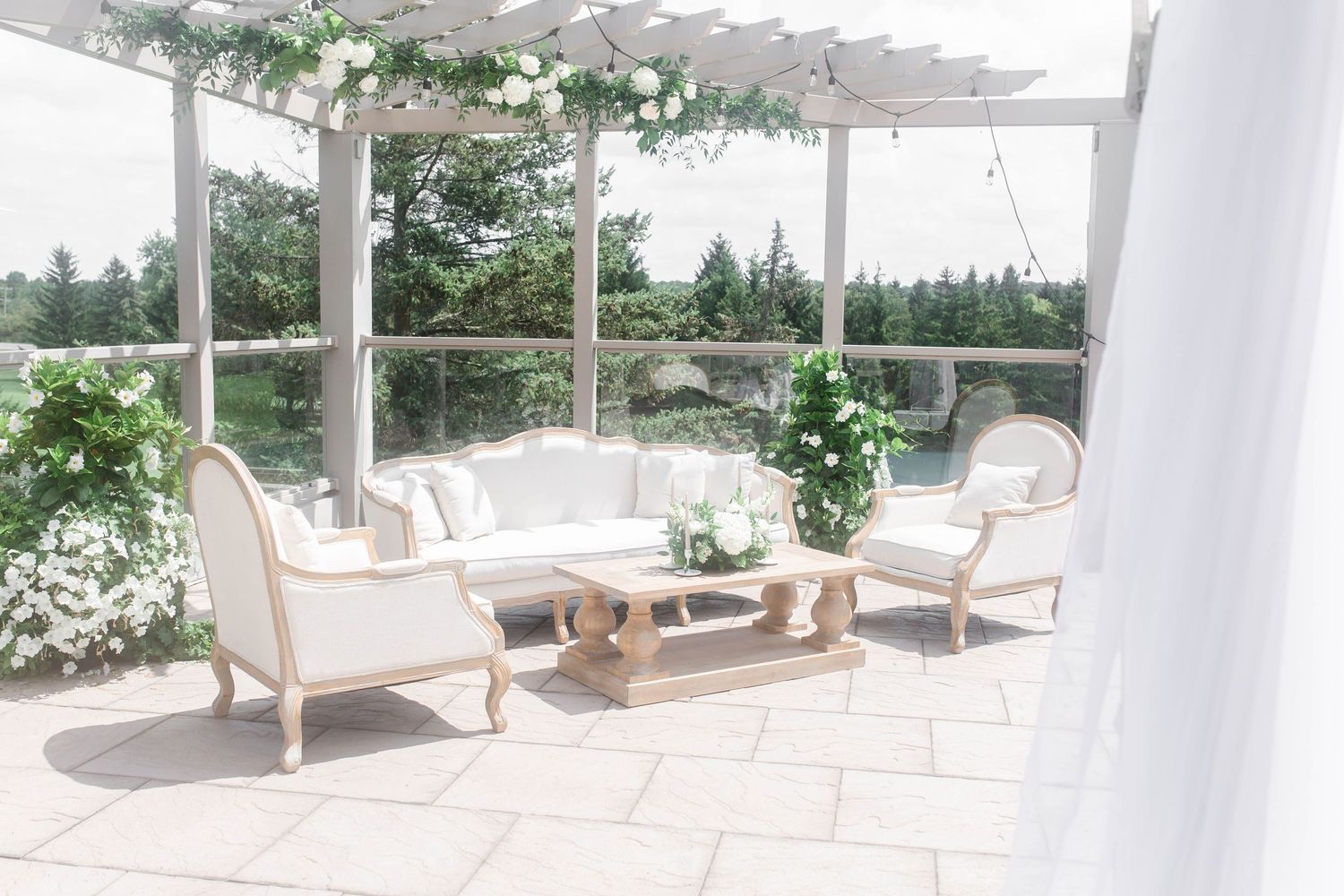Elegant outdoor seating area with white cushioned furniture and a pergola covered in climbing greenery.
