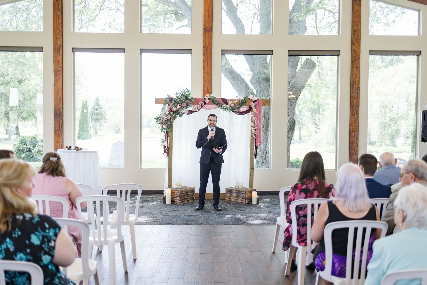 Light-filled wedding venue with white chairs and wooden beams set up for indoor ceremony.