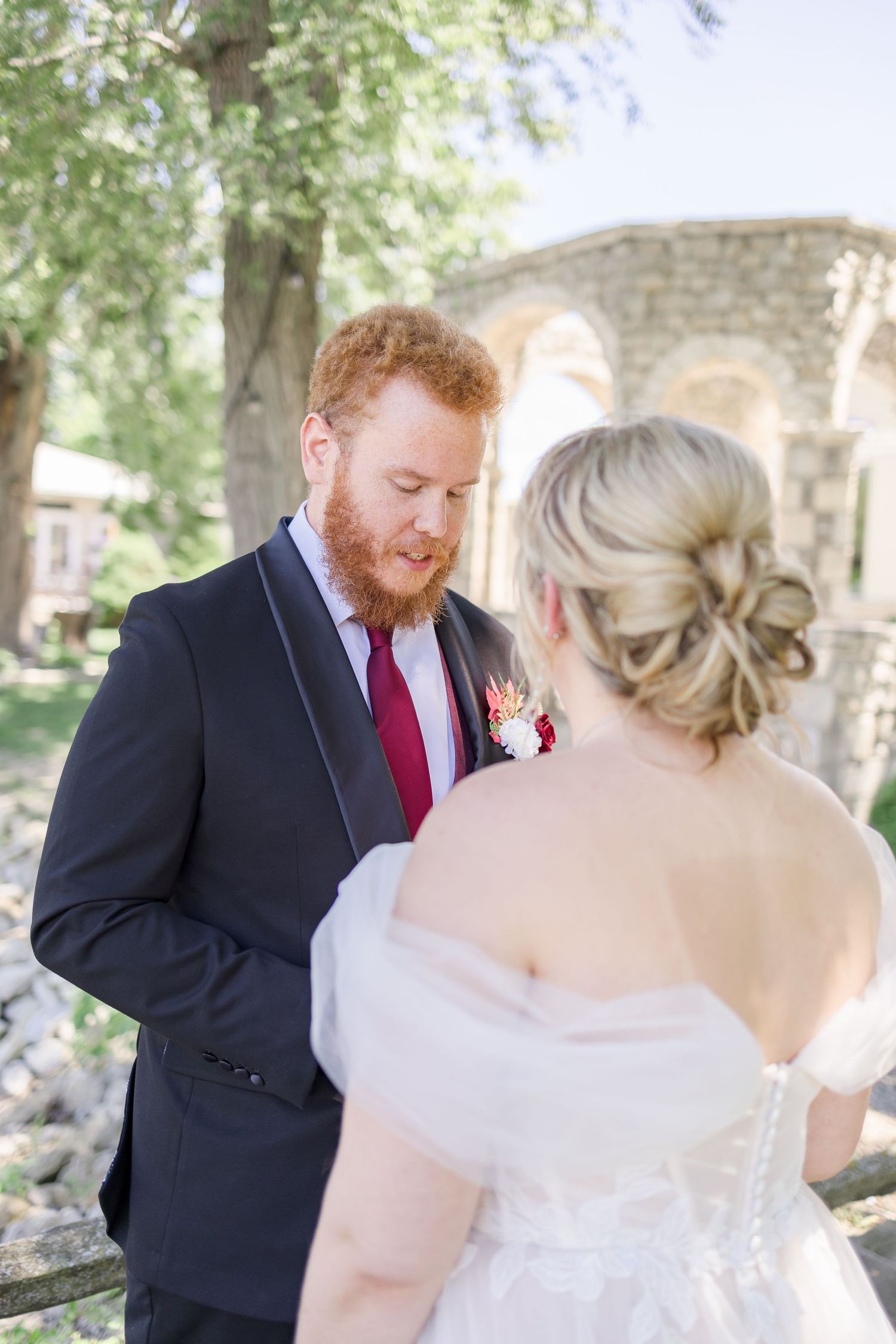 First look wedding moment captured in a garden setting with stone architecture.