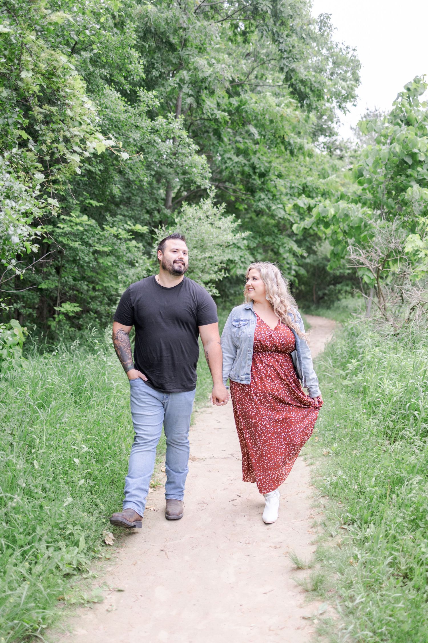 Couple walking hand in hand along a nature trail surrounded by green foliage.