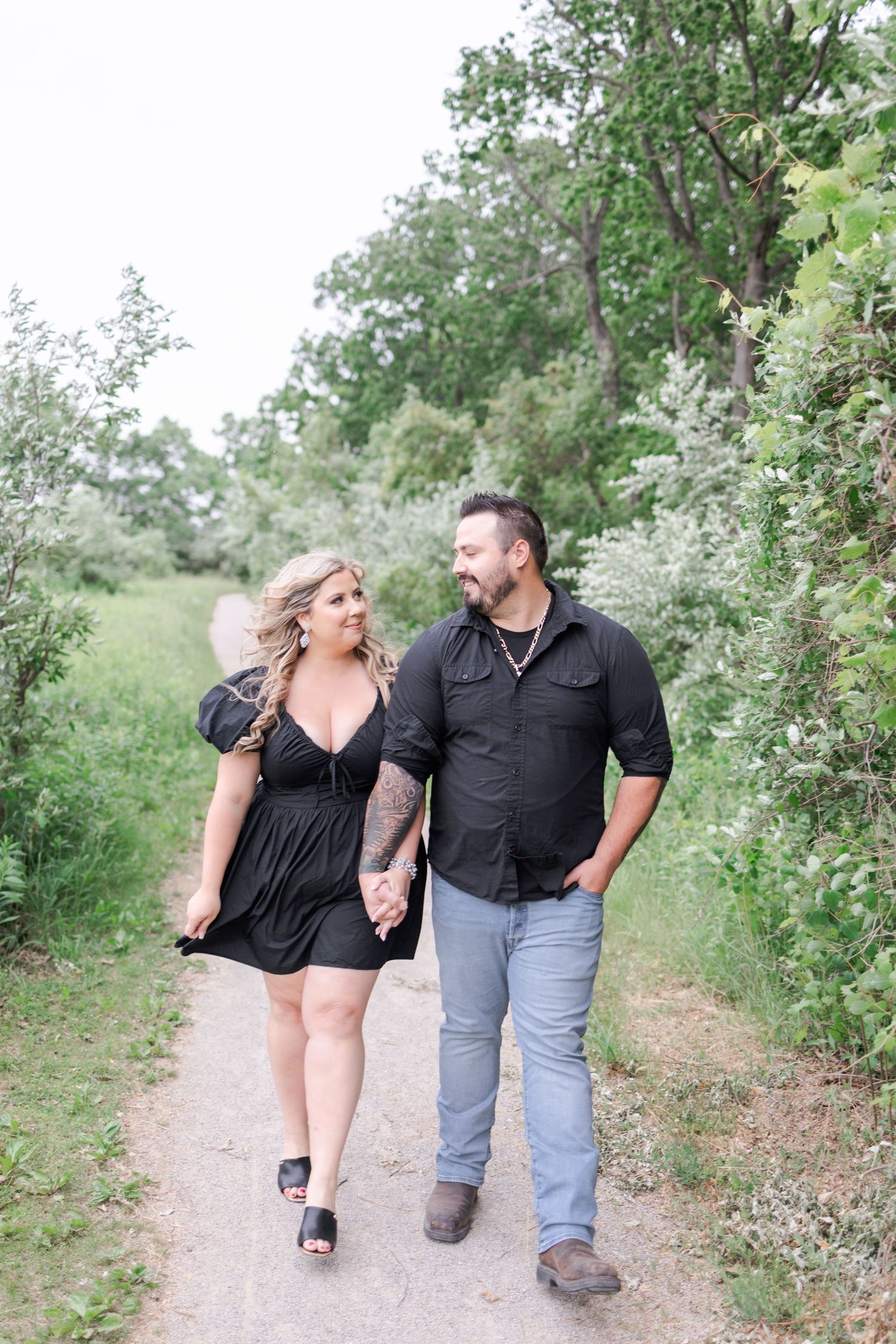 Couple walking together on a nature trail surrounded by green foliage.
