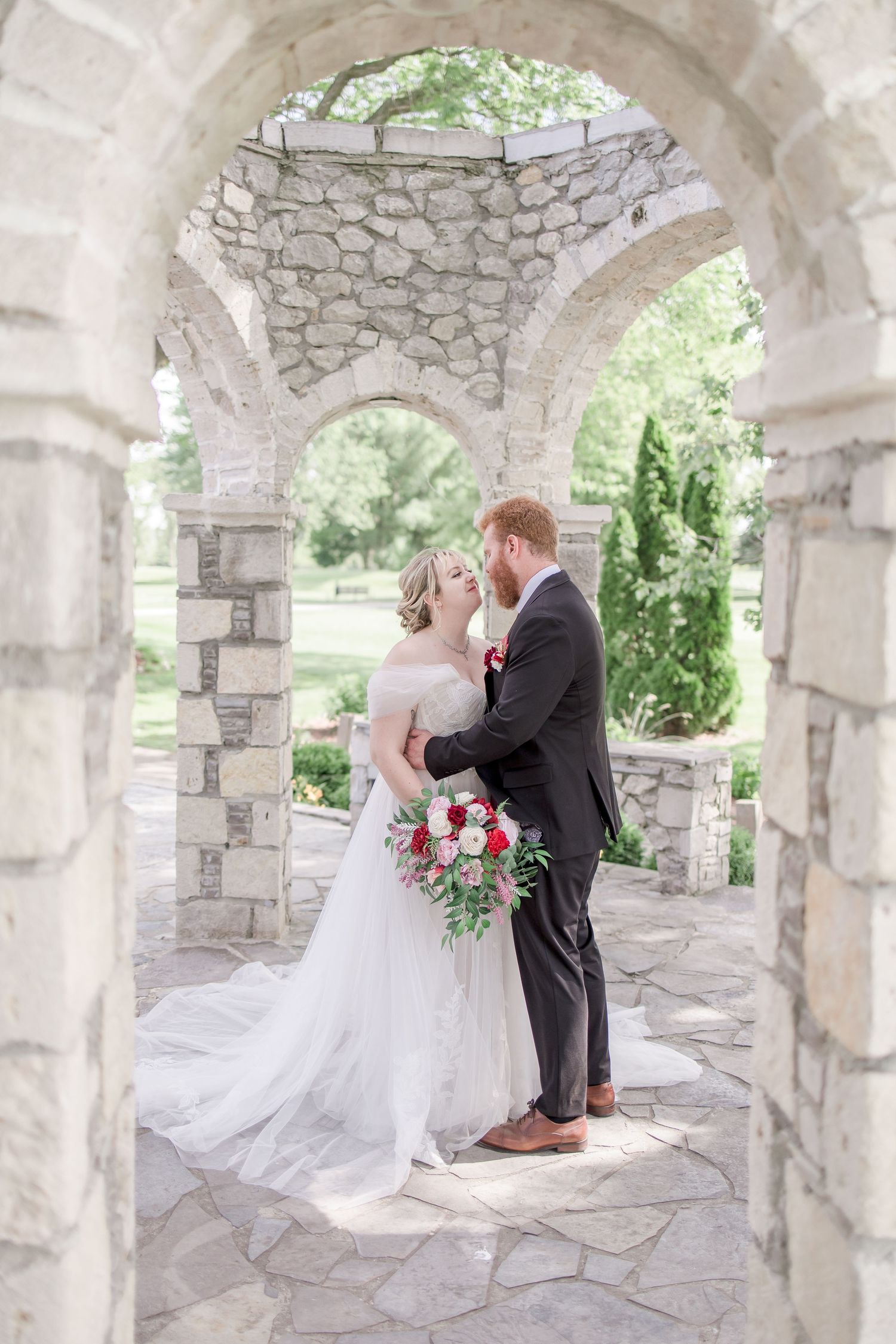 Bride and groom share tender moments beneath stone colonnade with floral accents.