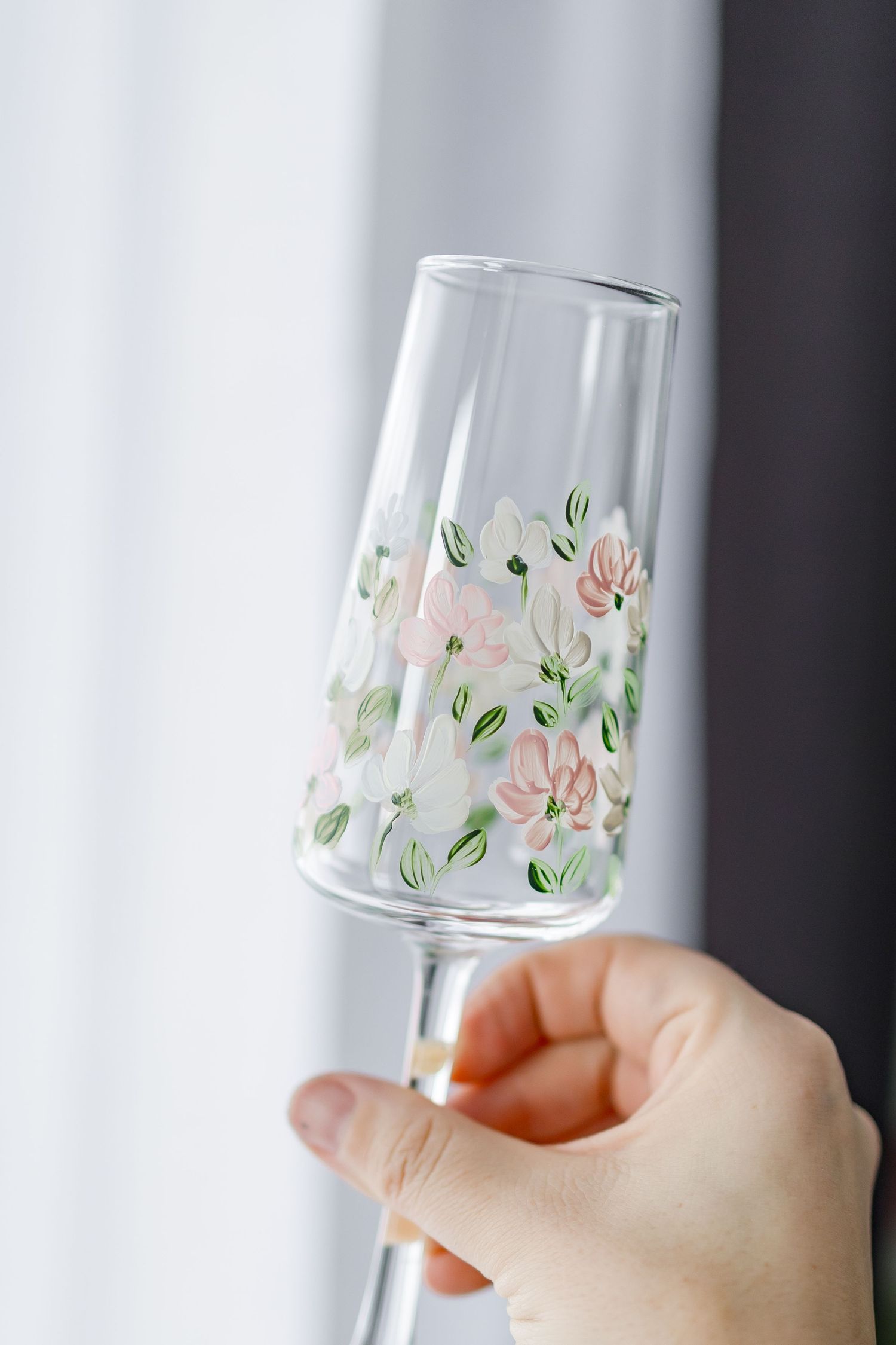Hand holding a delicate champagne glass with pink floral pattern painted on clear glass.