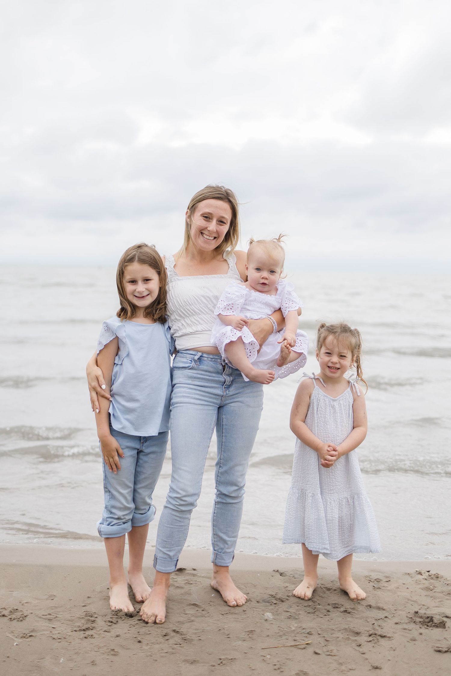 Family group standing barefoot on beach in coordinated casual outfits.