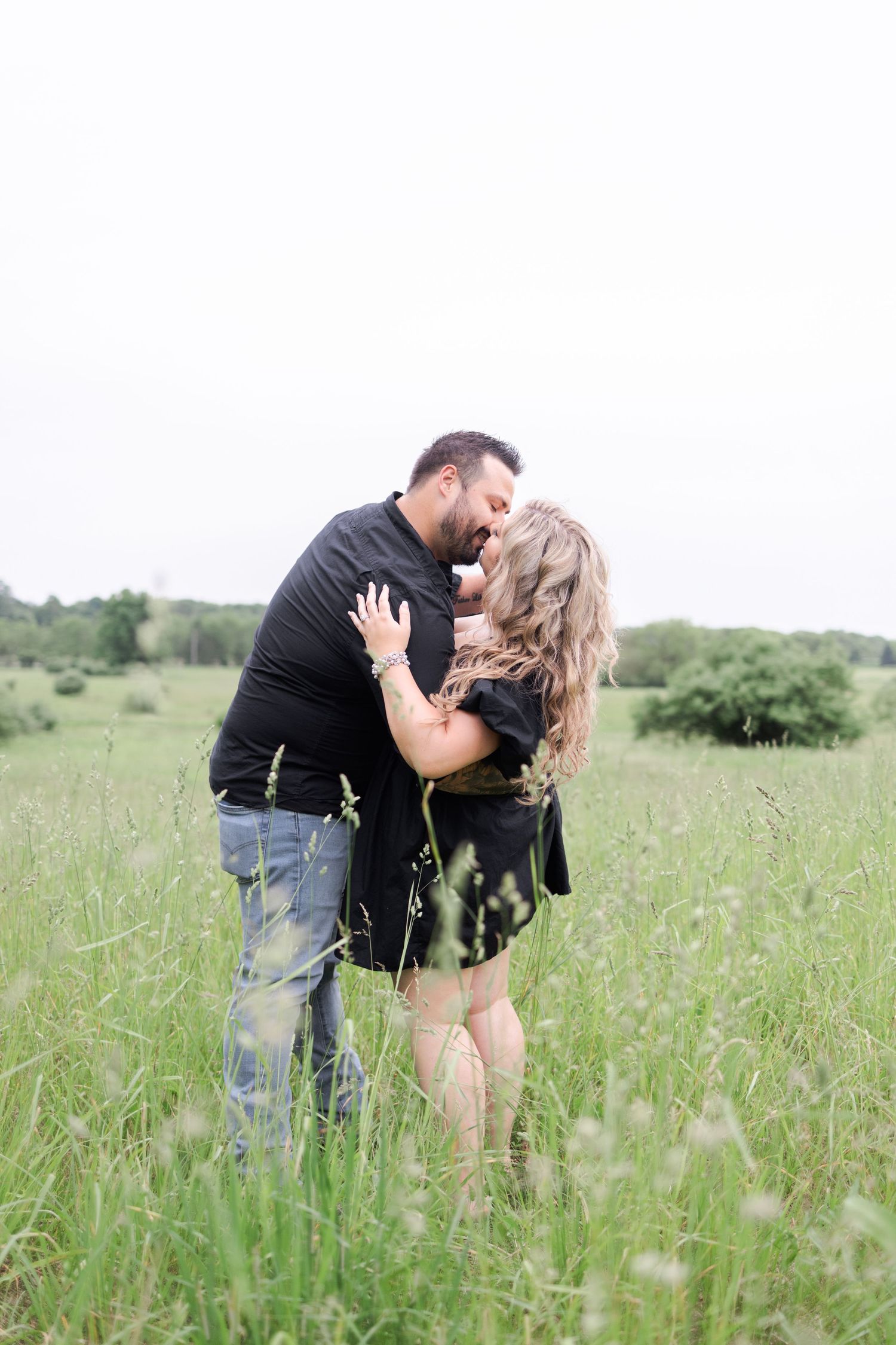 A couple shares romantic moments while standing in a sunlit meadow.