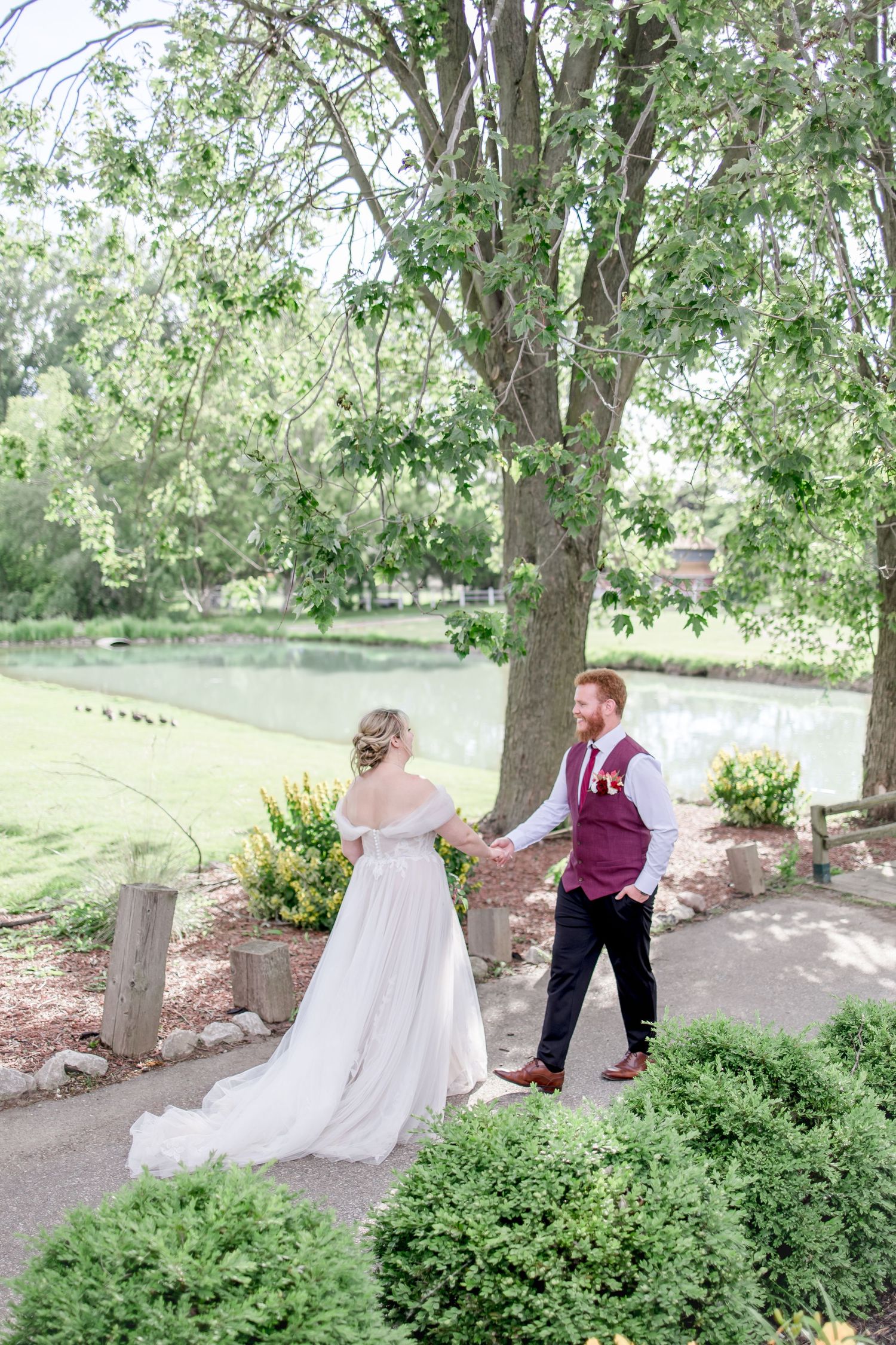 Couple taking romantic outdoor wedding photos along garden path with trees in background.
