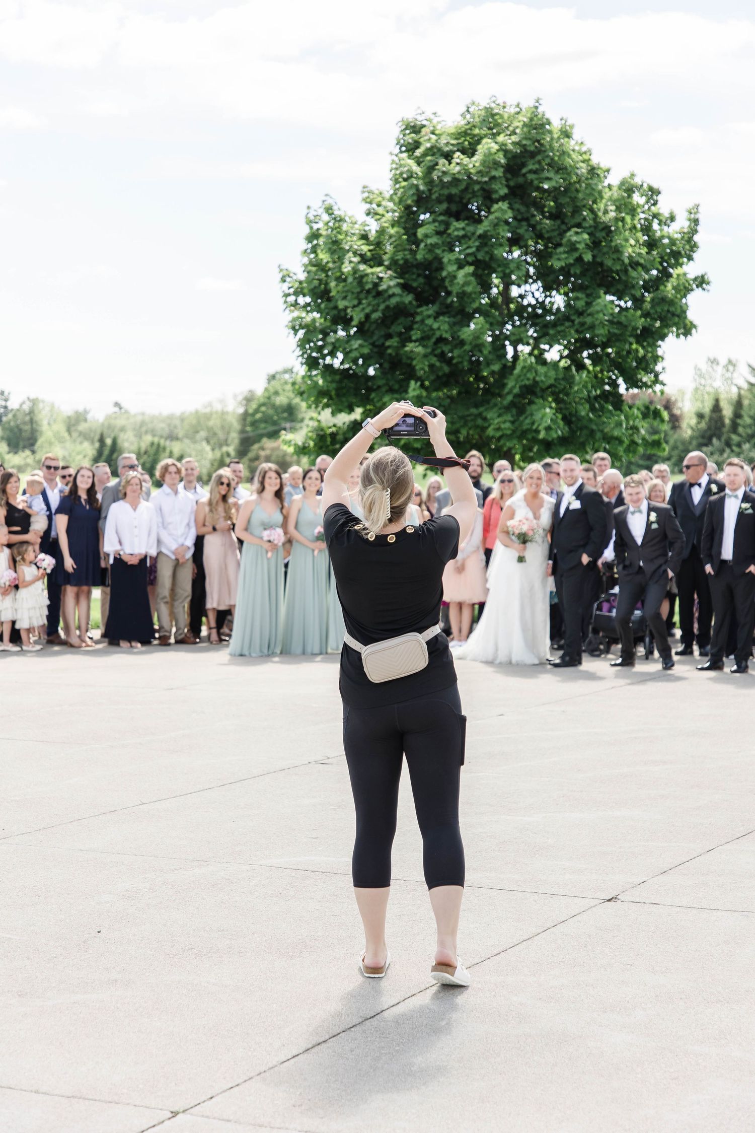 A wedding photographer captures a large group photo of guests outdoors.
