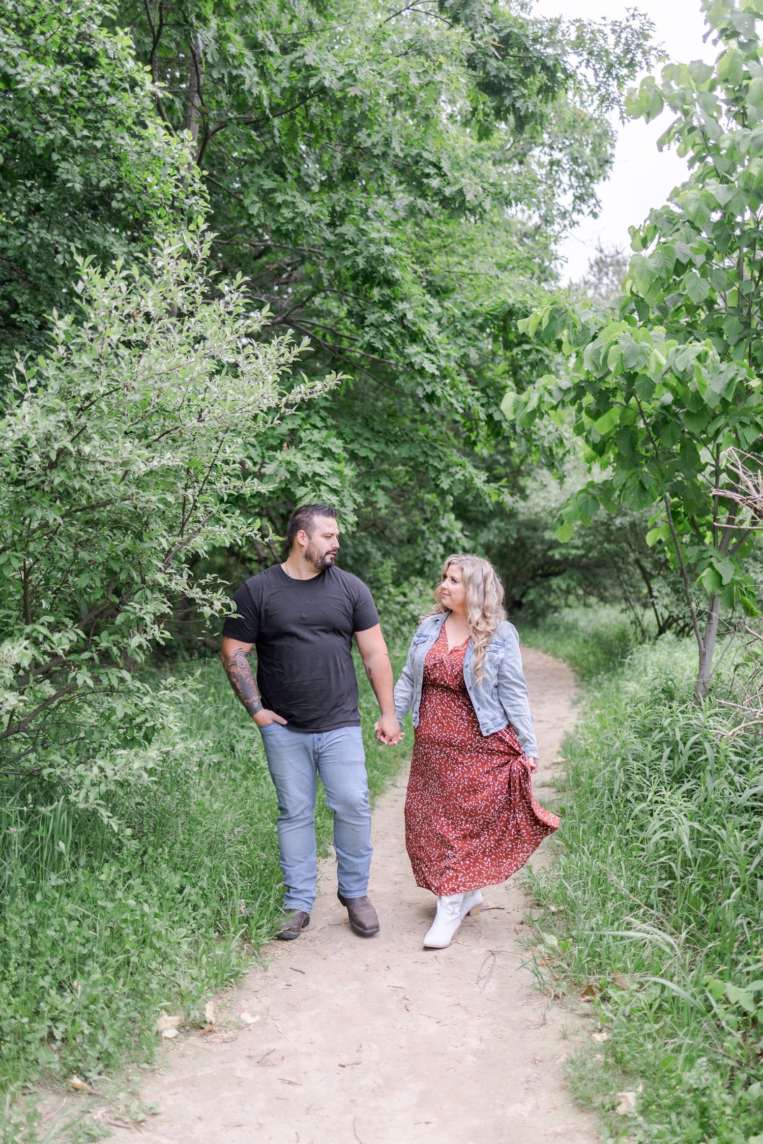 Two people strolling together on a dirt path lined with lush summer vegetation.