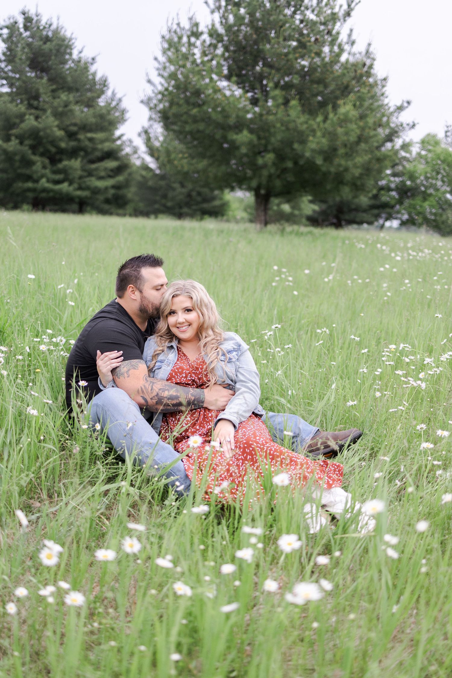 A romantic couple relaxes in a summer meadow filled with white wildflowers and tall grass.
