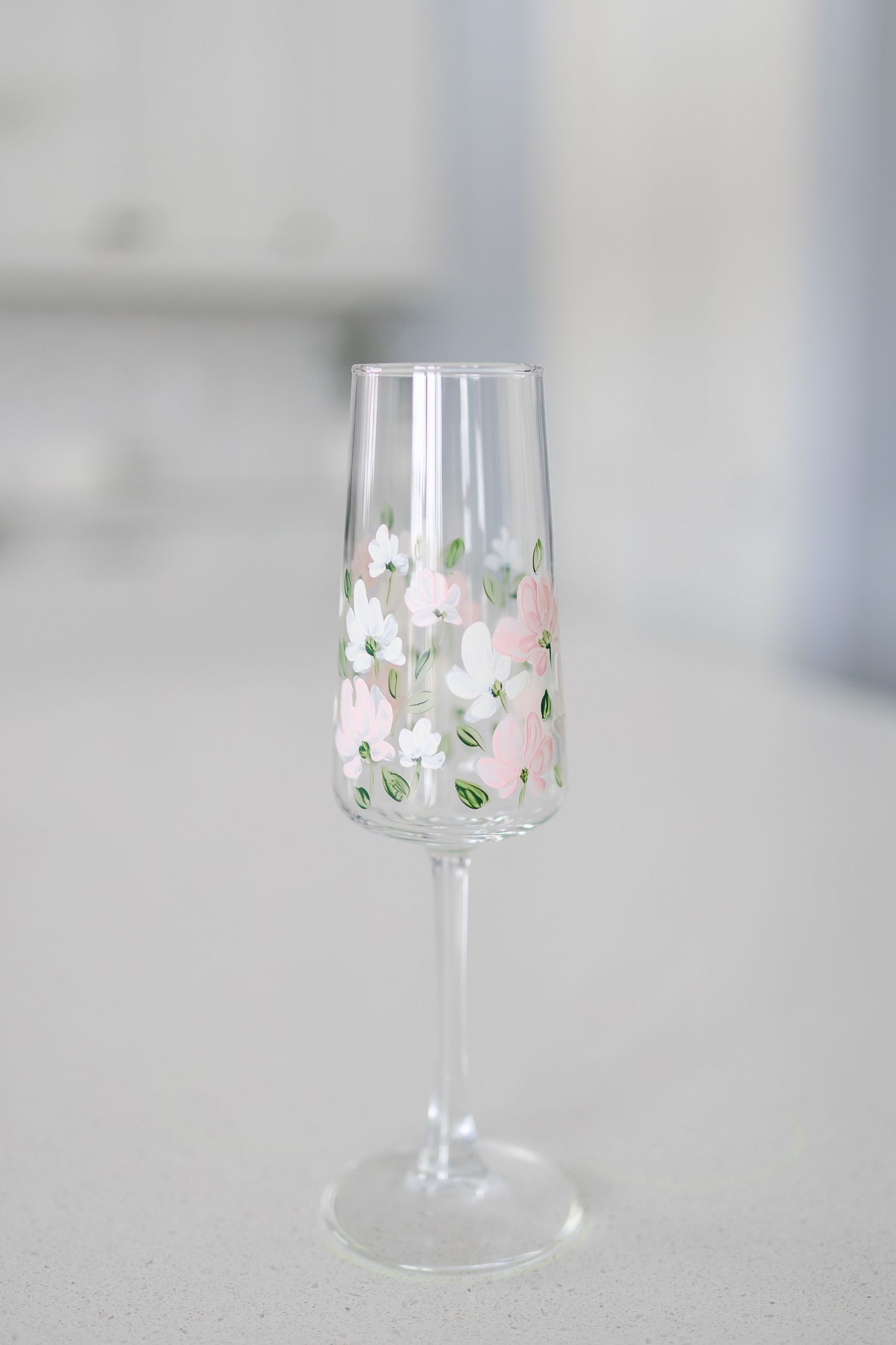 A delicate wine glass with pink and white floral decorative pattern on clear crystal against a light gray background.