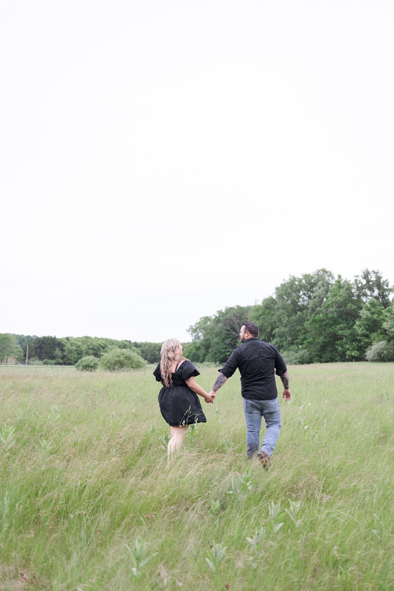 Two people chase each other through tall grass in an open field.
