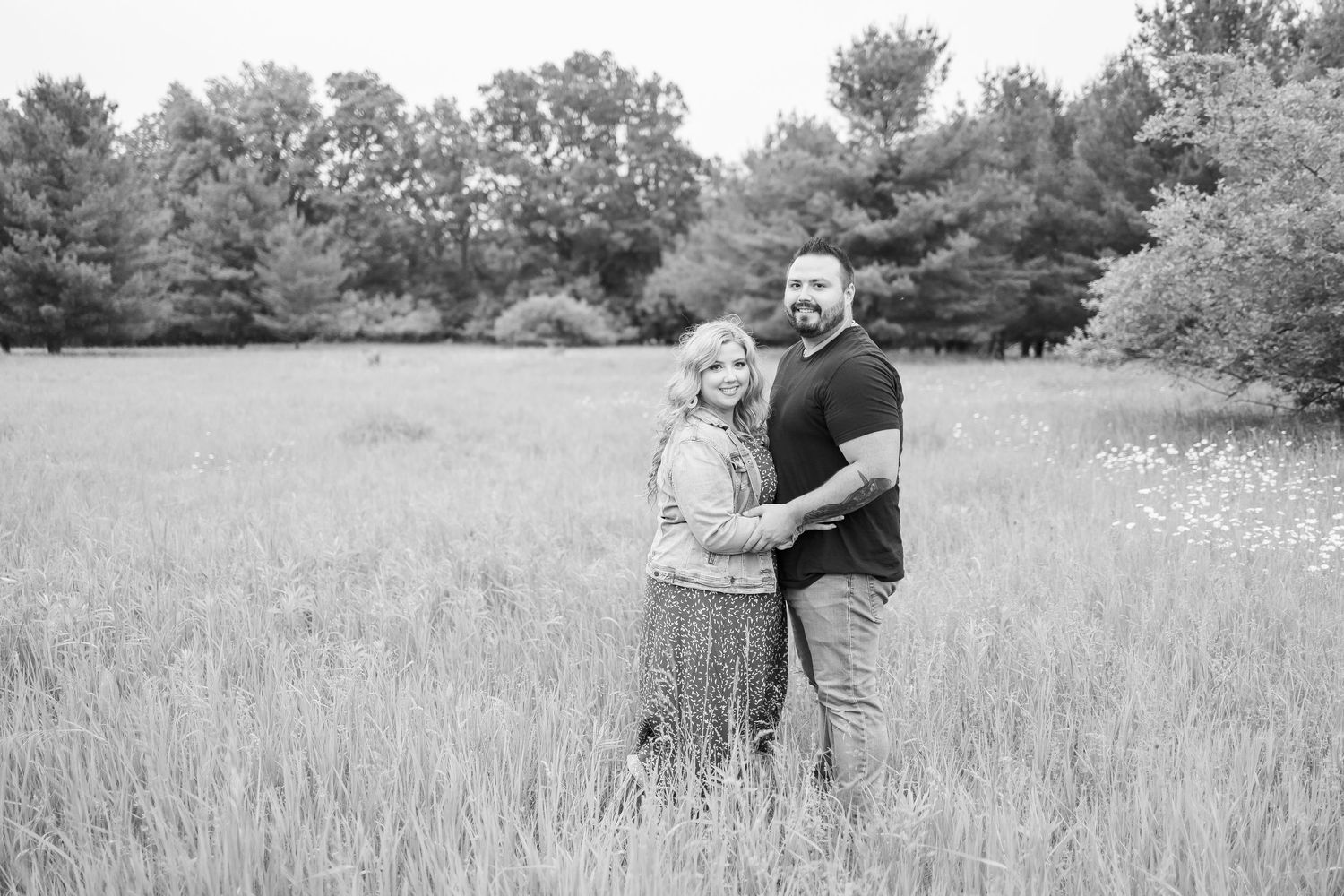 Couple sharing an intimate moment in a vast field surrounded by evergreen trees.
