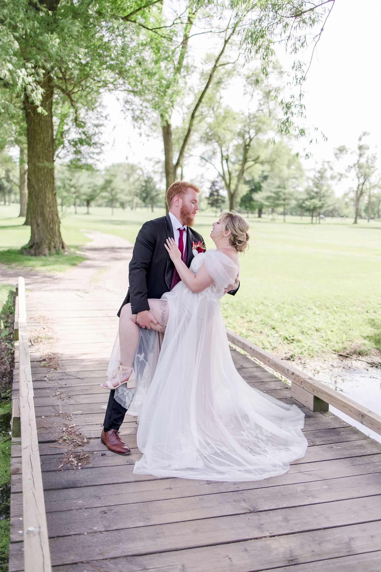 Wedding couple sitting together on rustic wooden bridge in outdoor garden setting.