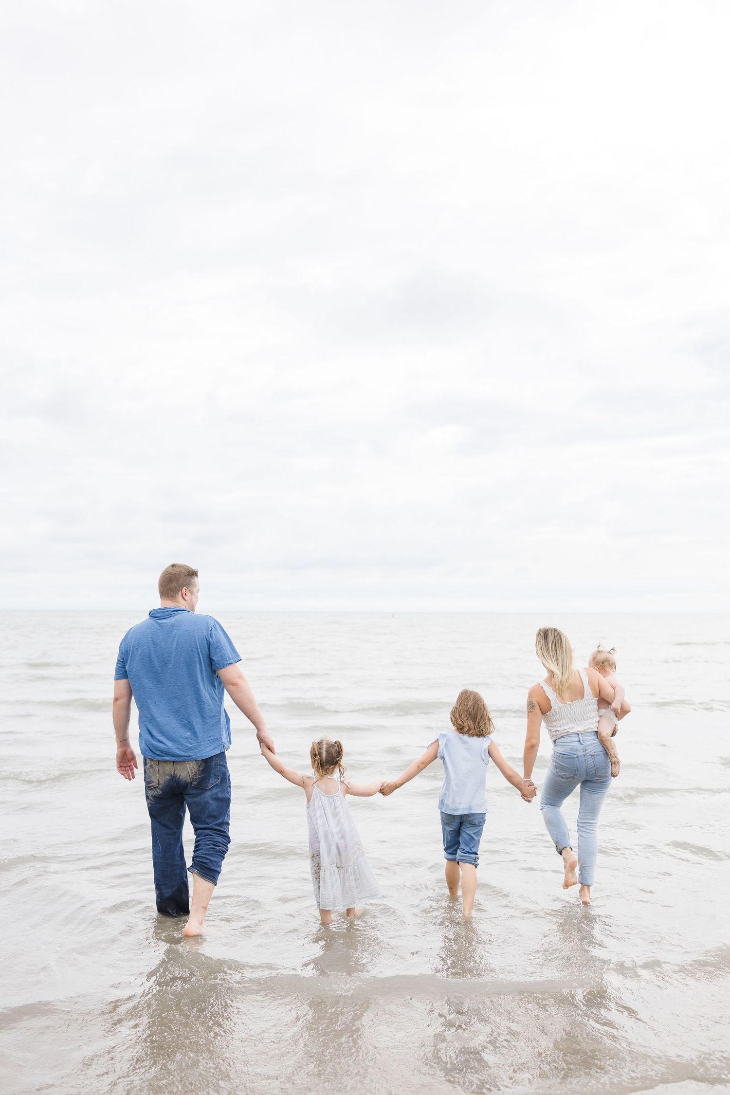 Family walking together holding hands in the ocean waves at the beach.