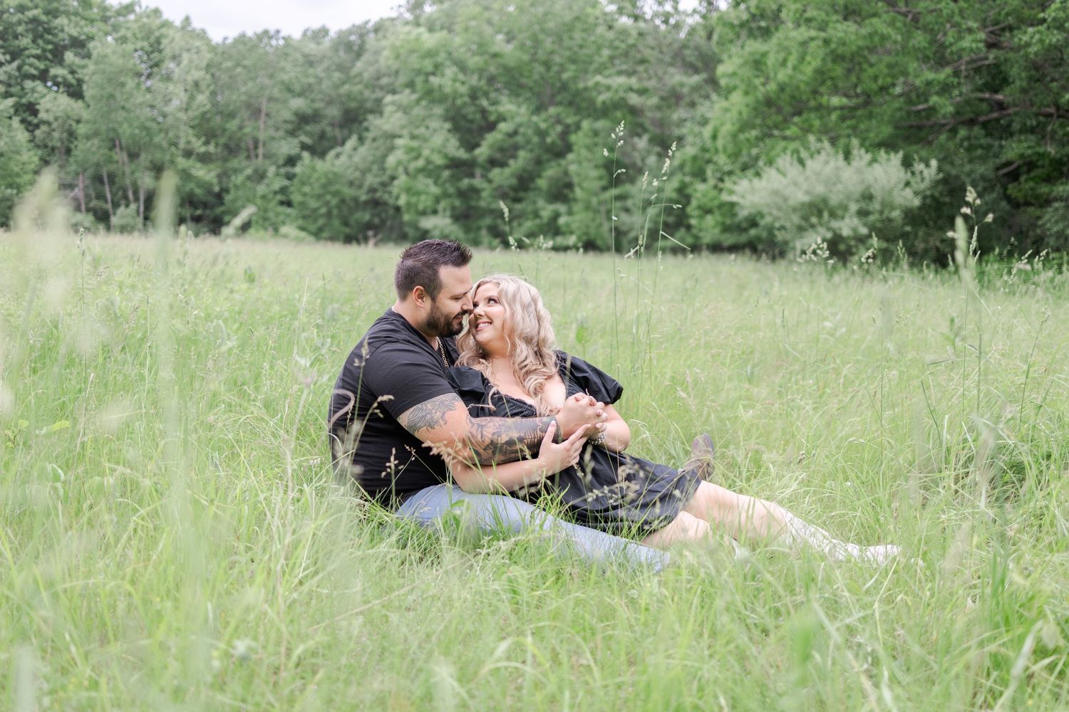 Couple lying in a grassy meadow surrounded by wildflowers and greenery on a sunny day.