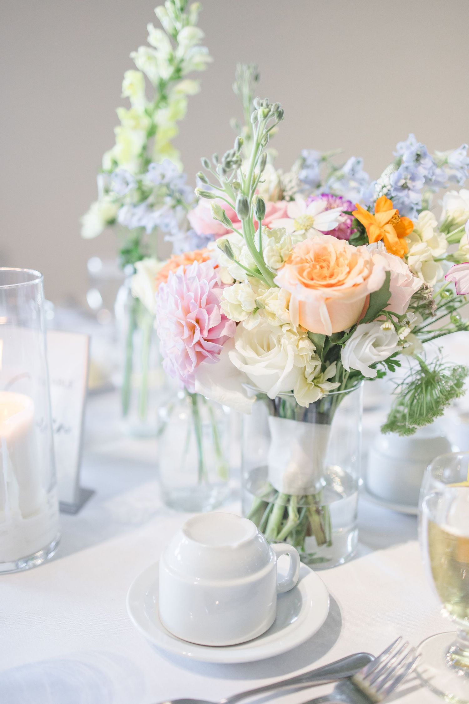 Elegant wedding table setting with pastel floral centerpieces in glass vases.