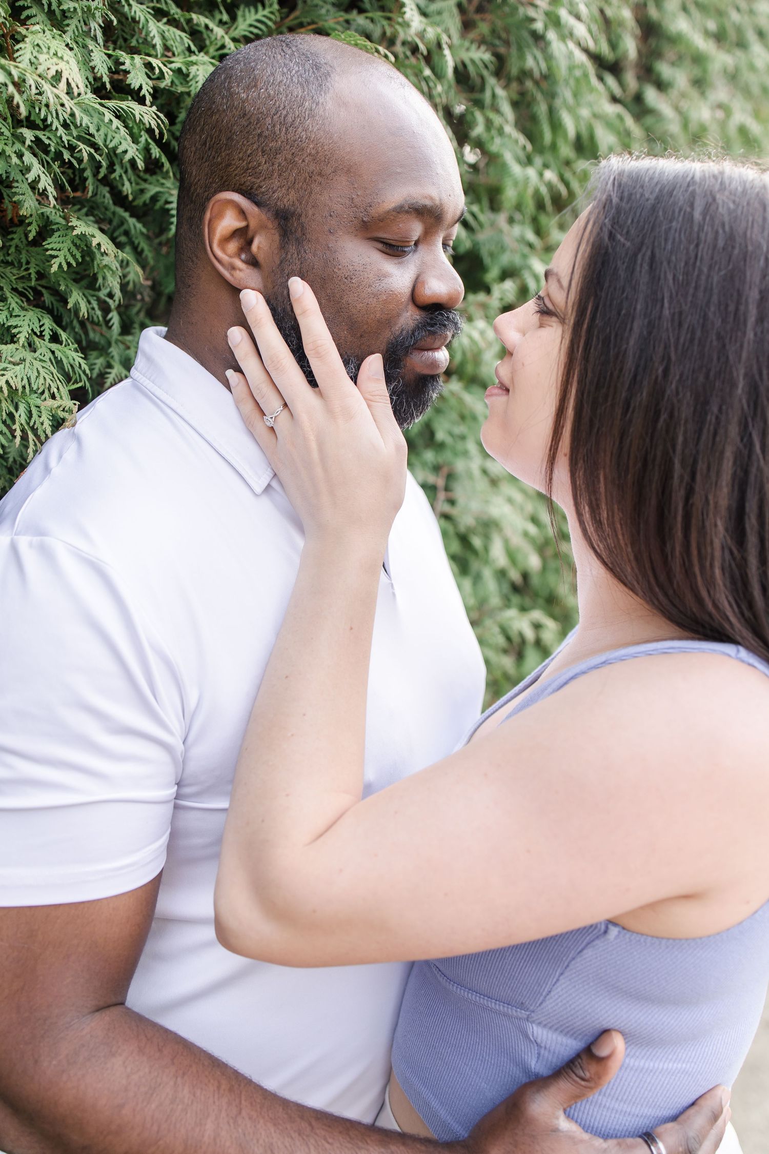 A romantic couple embraces in front of lush green foliage during an intimate outdoor photoshoot.
