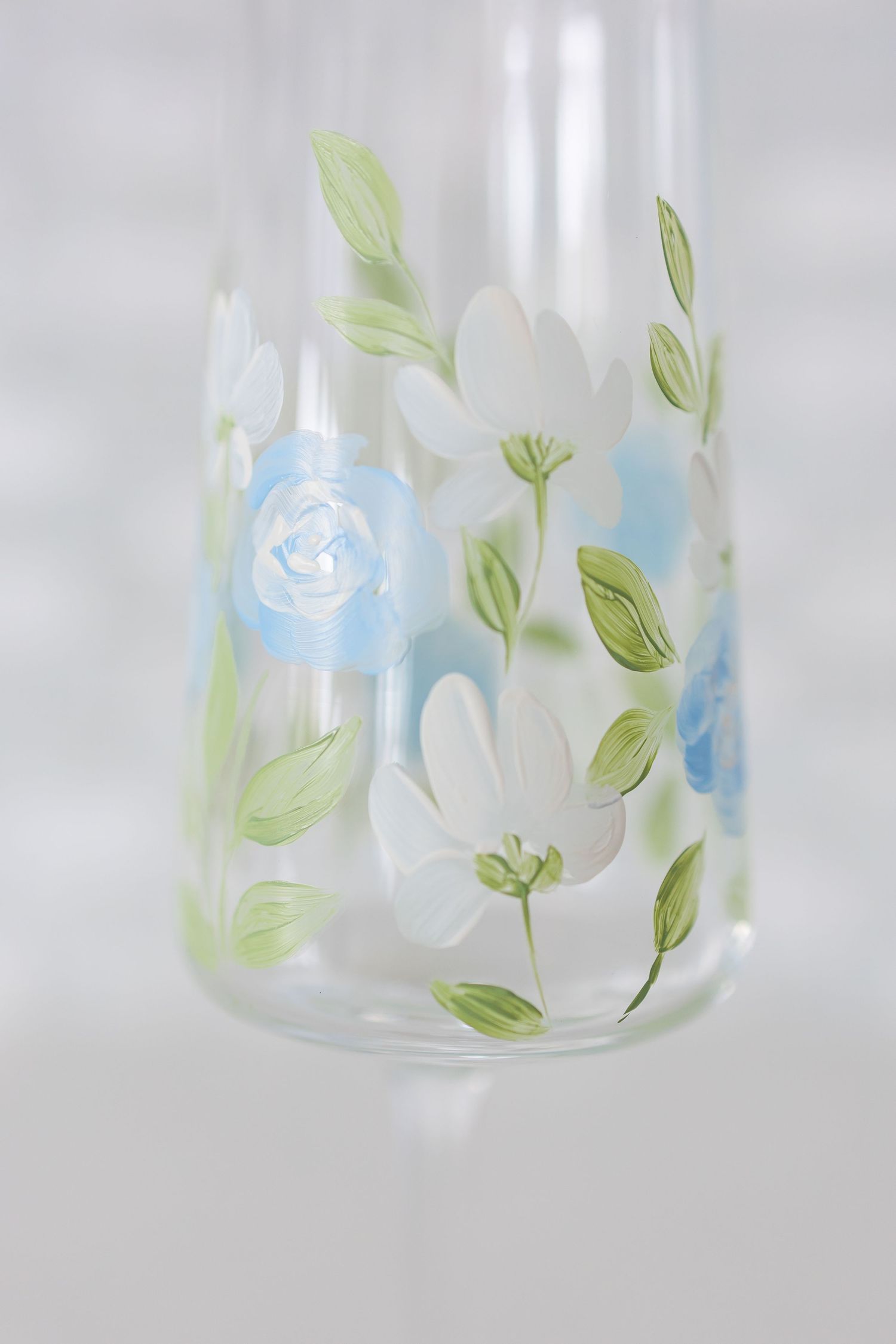 Clear glass jar with delicate blue flowers and green leaves painted in a whimsical pattern around the rim.