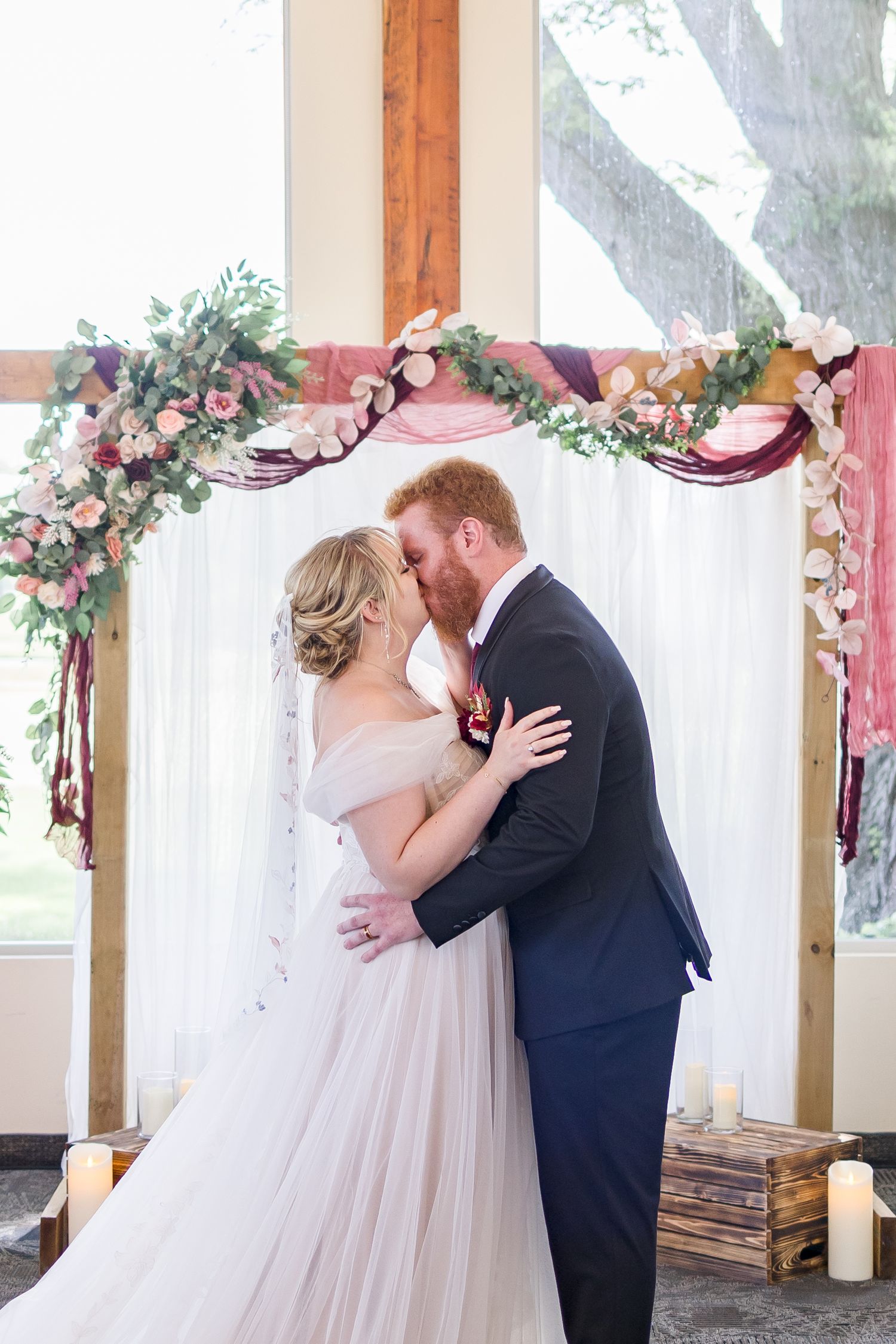 Romantic first look moment under floral arch in sunlit indoor venue.