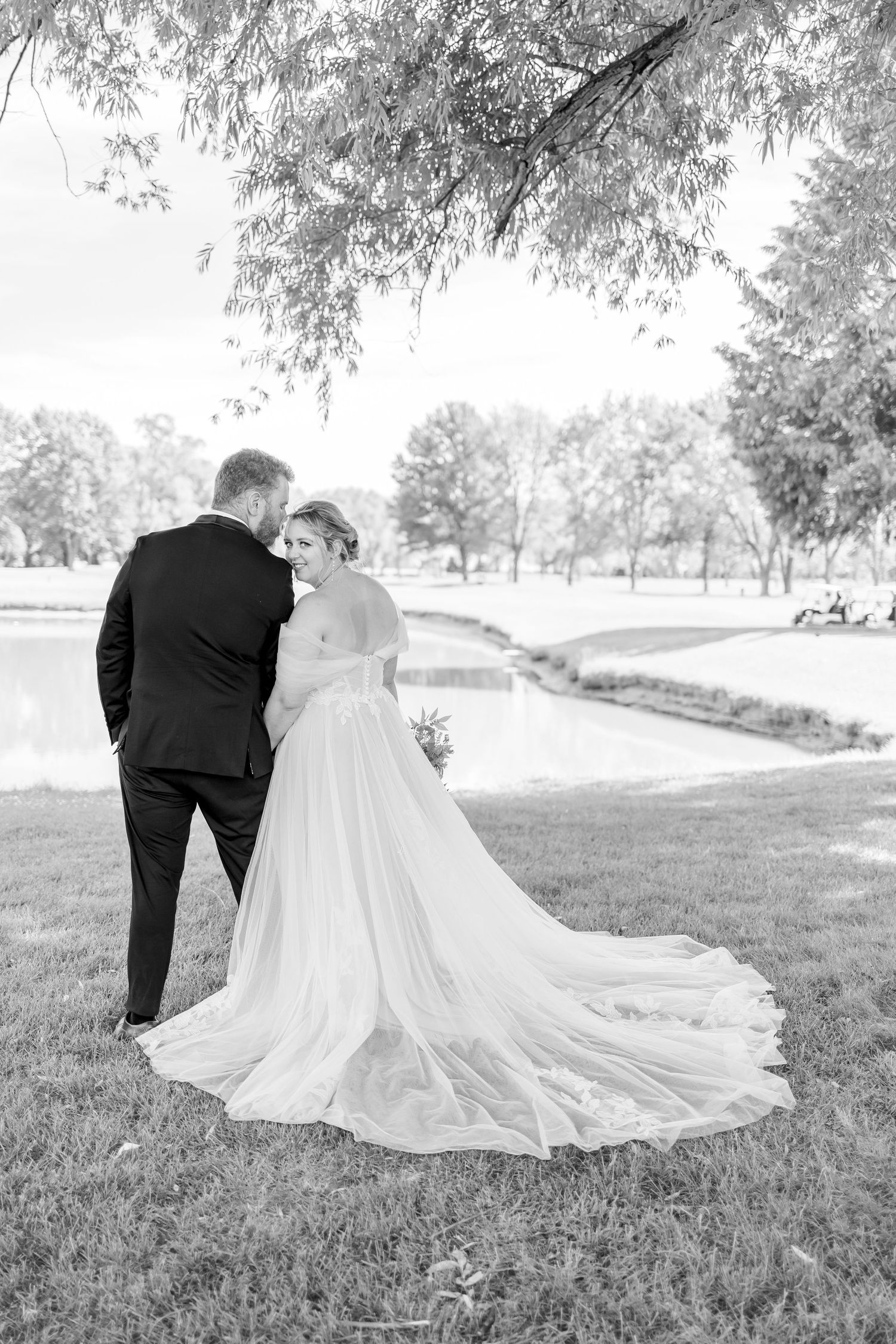 Black and white wedding photo showing couple on grassy hillside.