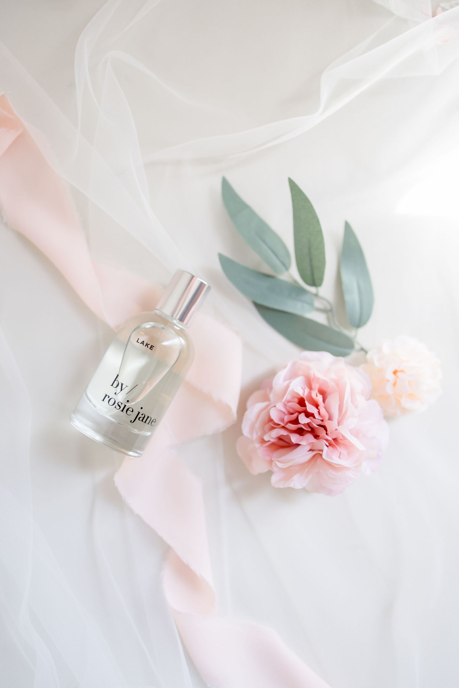 Elegant perfume bottle with pink carnation and ribbon on white fabric.