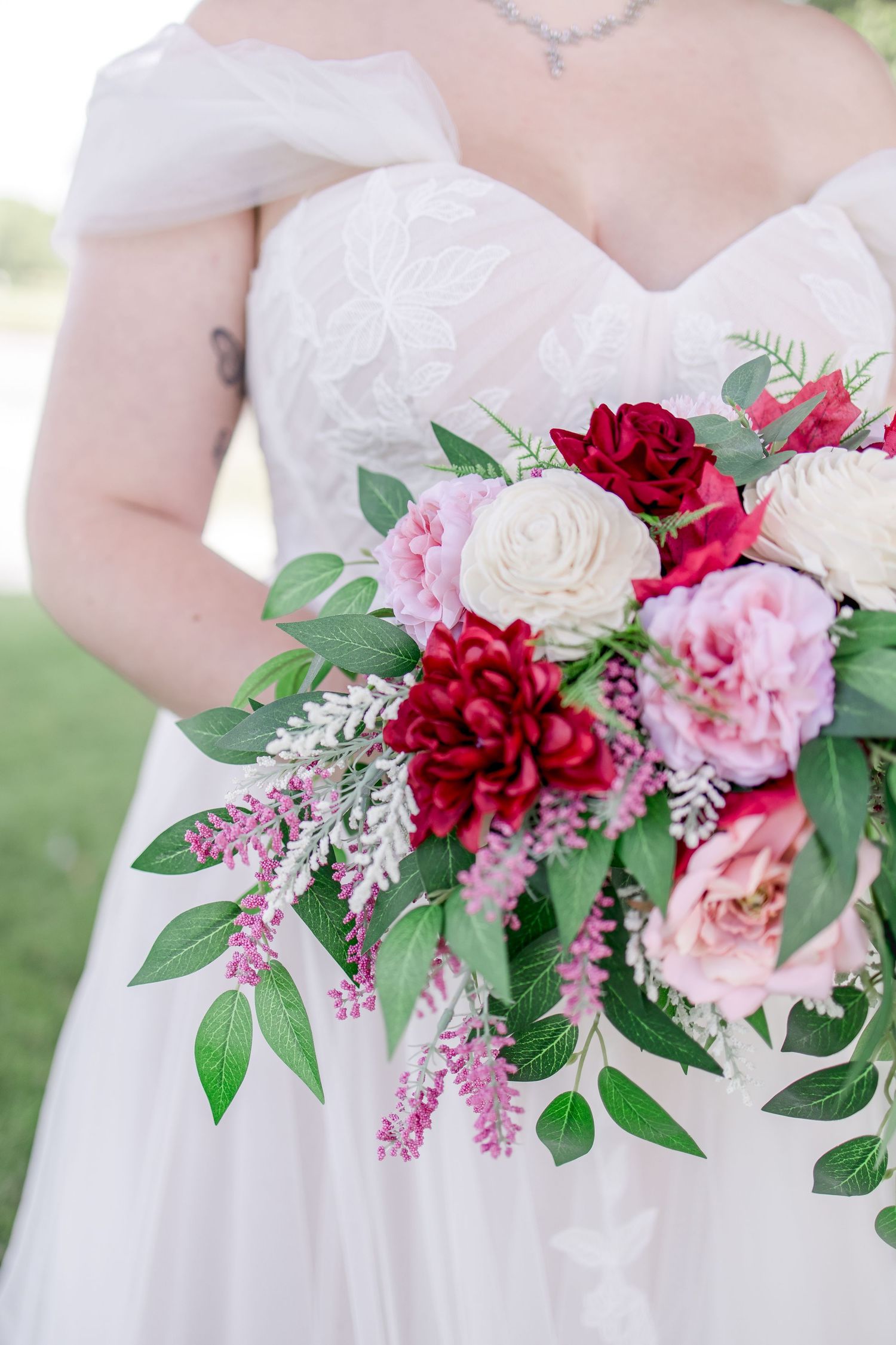 Close-up of bridal bouquet featuring red roses, pink flowers and green foliage.