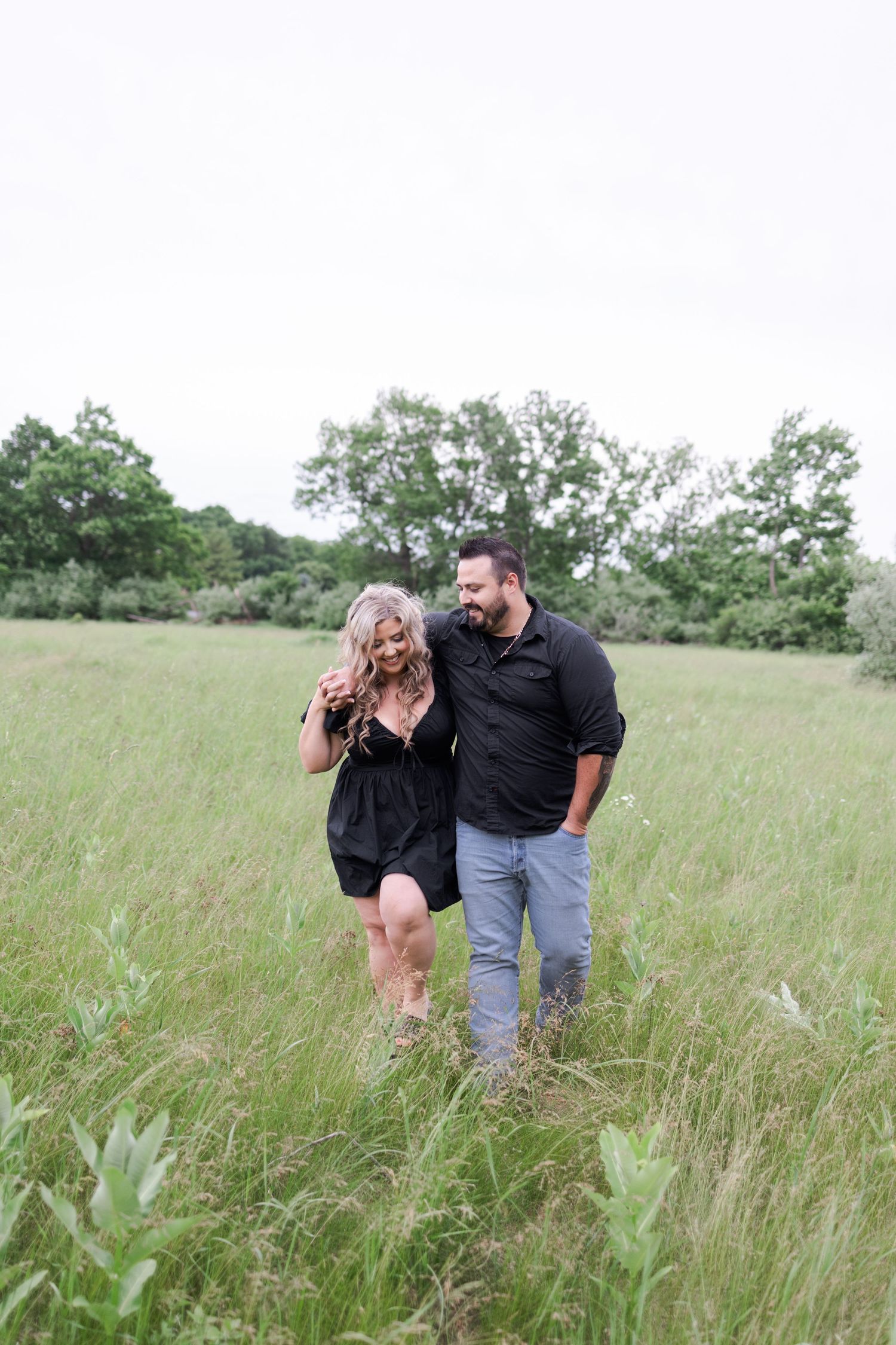 A couple enjoys a candid moment while walking through a grassy field.