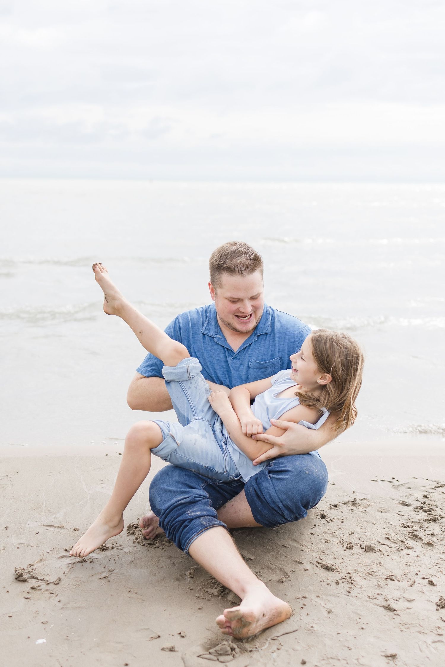 Playful interaction between parent and child on a cloudy beach day.